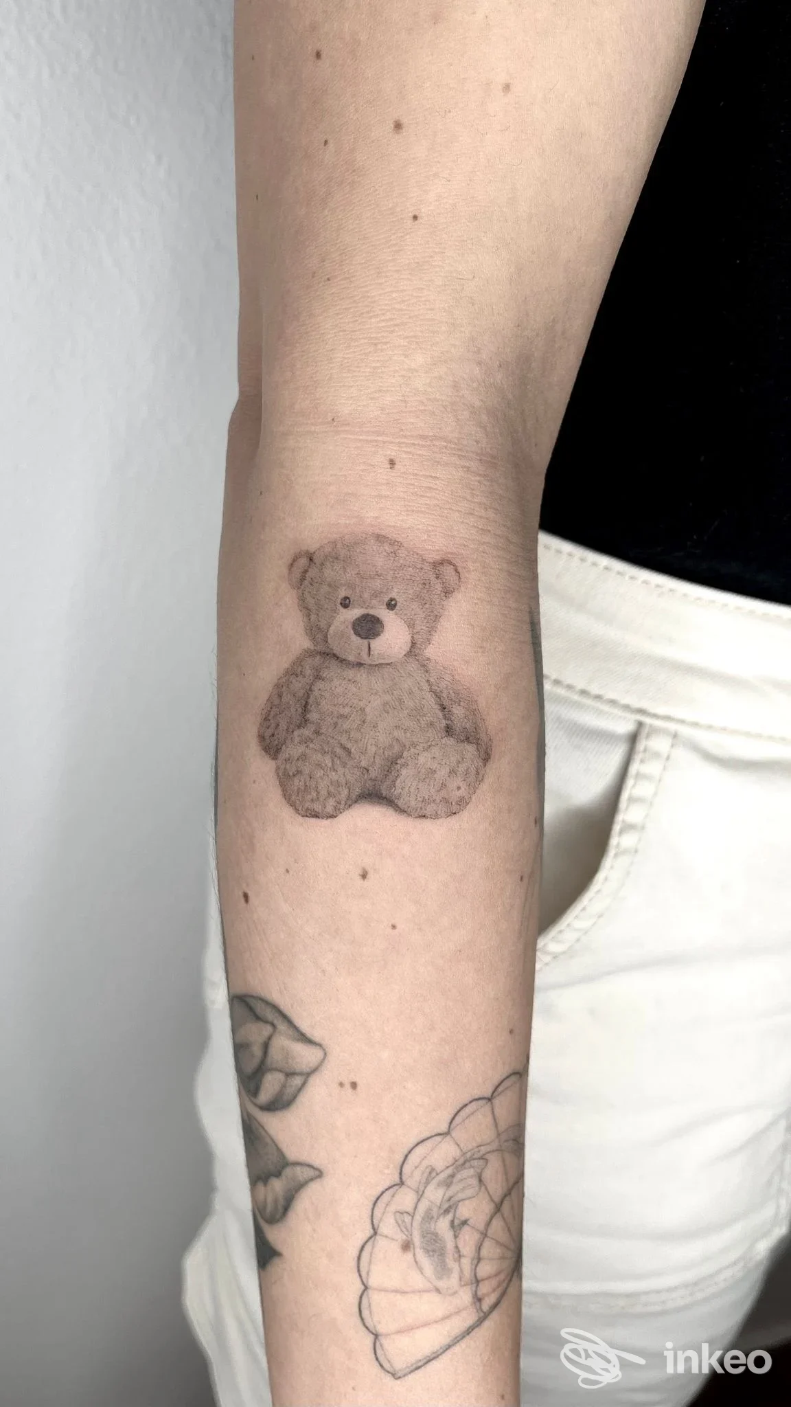 Tatuaggio su pelle reale di un piccolo orsetto grigio situato sull'avambraccio sinistro, ritratto in primo piano senza testo né elementi social.