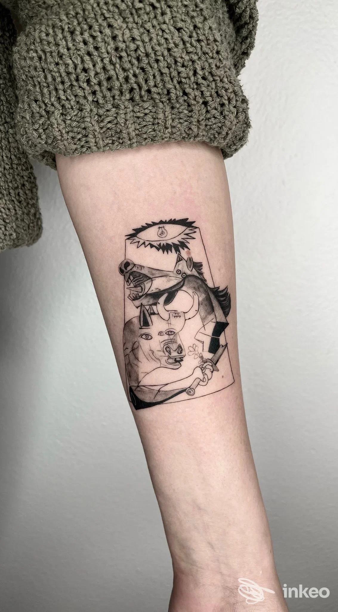 Tattoo sull'avambraccio sinistro: disegno stilizzato in bianco e nero con figure, all’interno di un contenitore, visibile su pelle nuda.