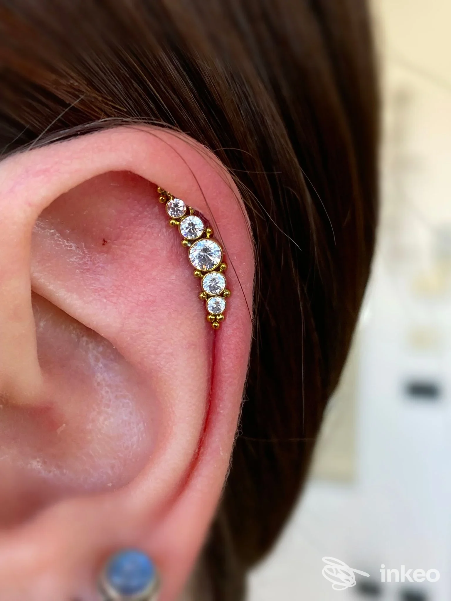 Orecchio sinistro con piercing lungo la cartilagine, decorato da pietre preziose dorate, visibile sulla pelle reale. Studio RavenVille Tattoo.