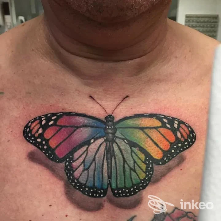 Tattoo a farfalla colorata sul petto, con ali multicolori e contorni scuri; nessun volto visibile.