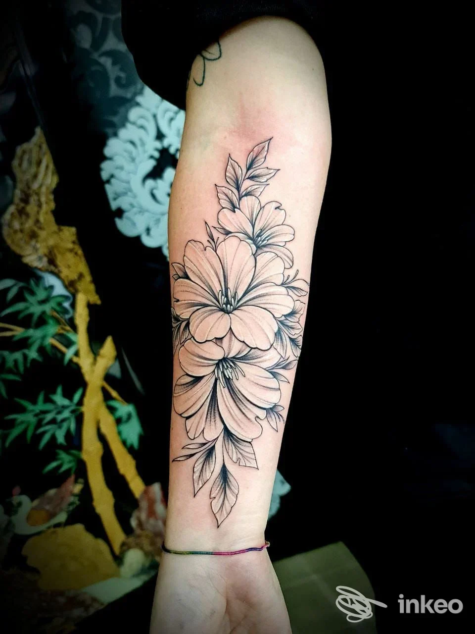 Tatuaggio floreale su avambraccio sinistro: grandi fiori e foglie in tratto lineare. Pelle ben definita, sfondo scuro. Nessun volto visibile.
