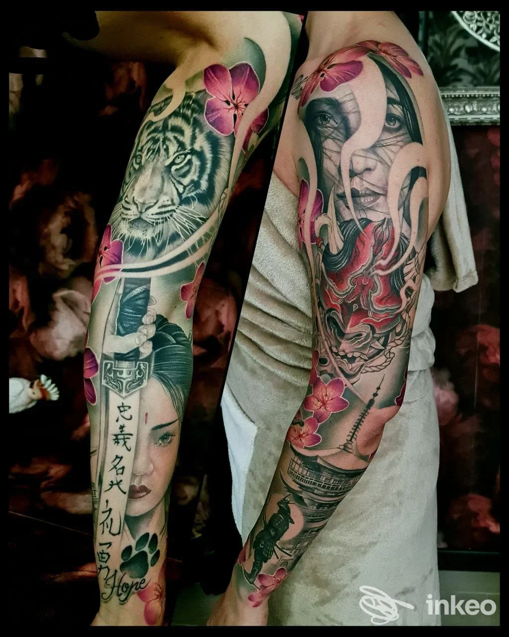 Due braccia tatuate appoggiate lateralmente, con colori vividi e motivi floreali e figure realistiche, sculture di fiori rosa e tigre su pelle reale, senza volti interi visibili.