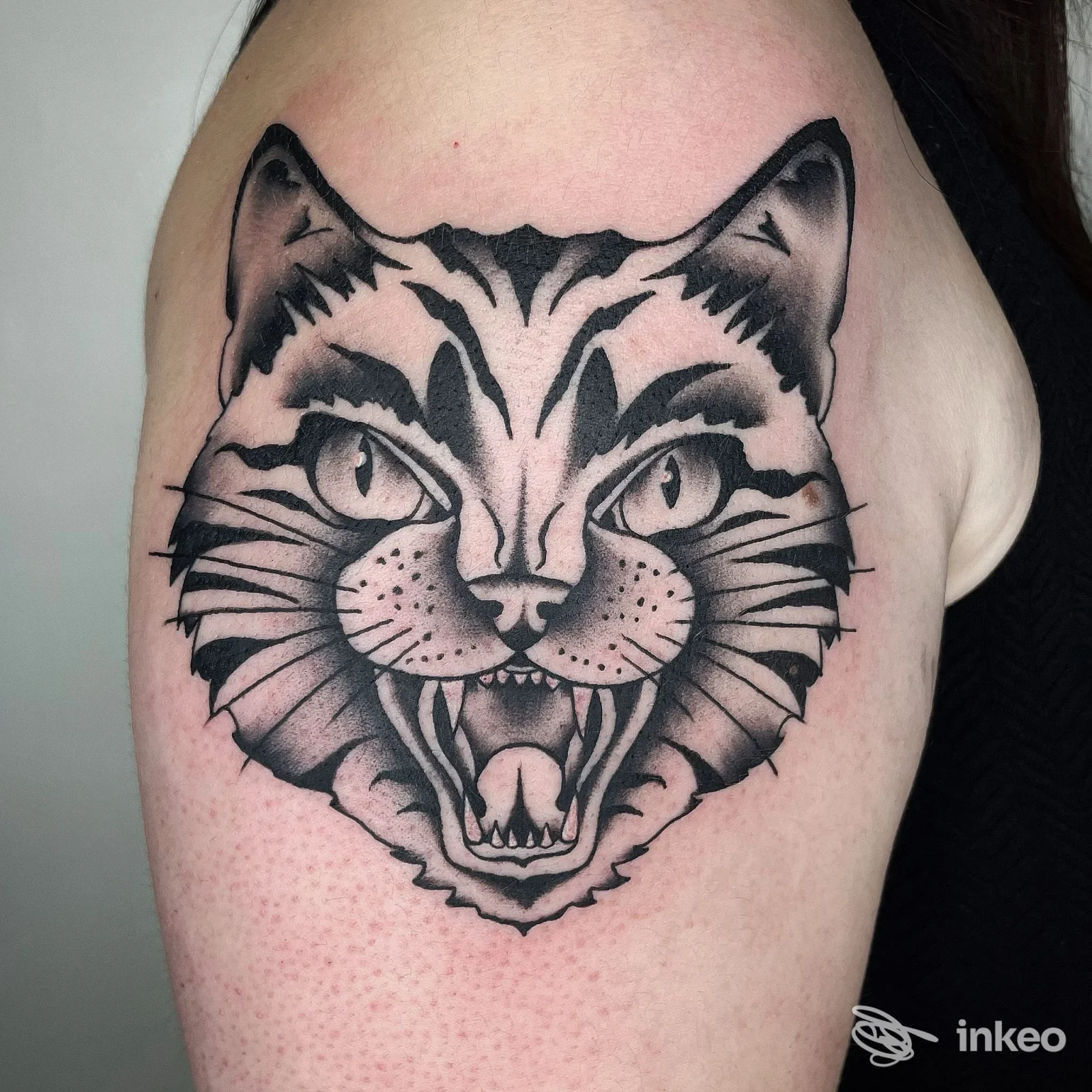 Tattoo realistico di una testa di gatto su braccio; linea nera e sfumature, senza testo o overlay visivo.