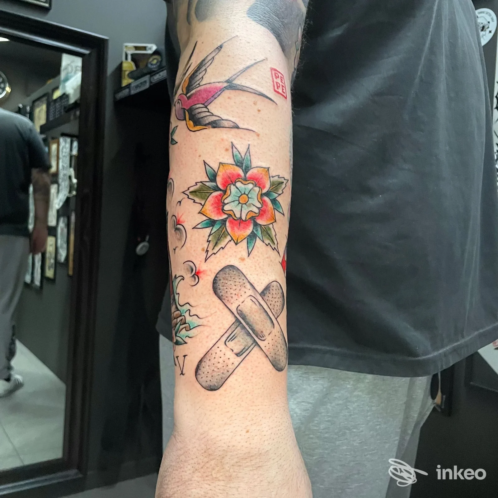 Avambraccio di una persona con un tatuaggio colorato a tema floreale e motivi di cerotto, visibile in primo piano nello studio.