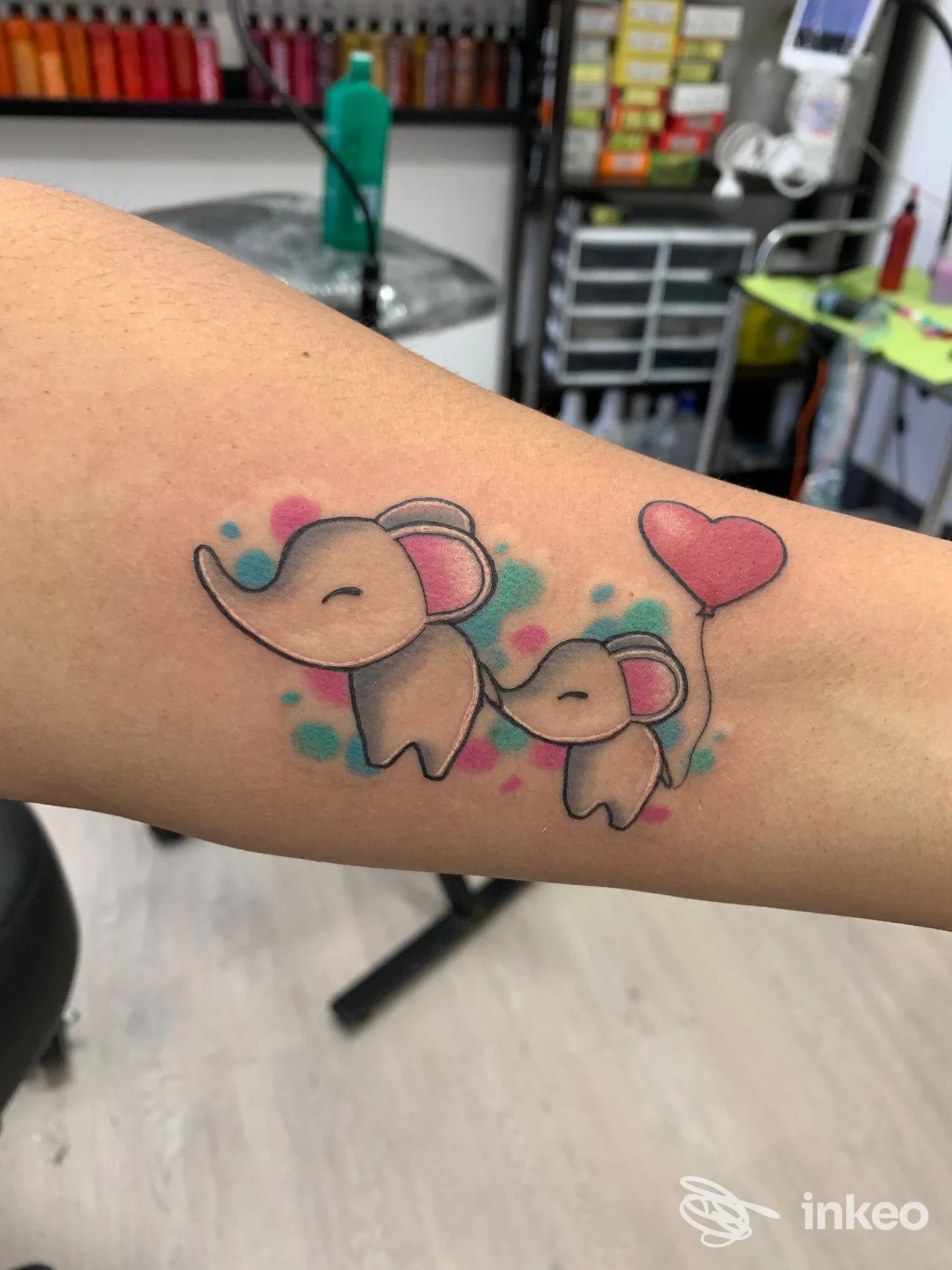 Due delicati elefanti tatuati sulla pelle, con un piccolo elefante e un palloncino a cuore, su un avambraccio.