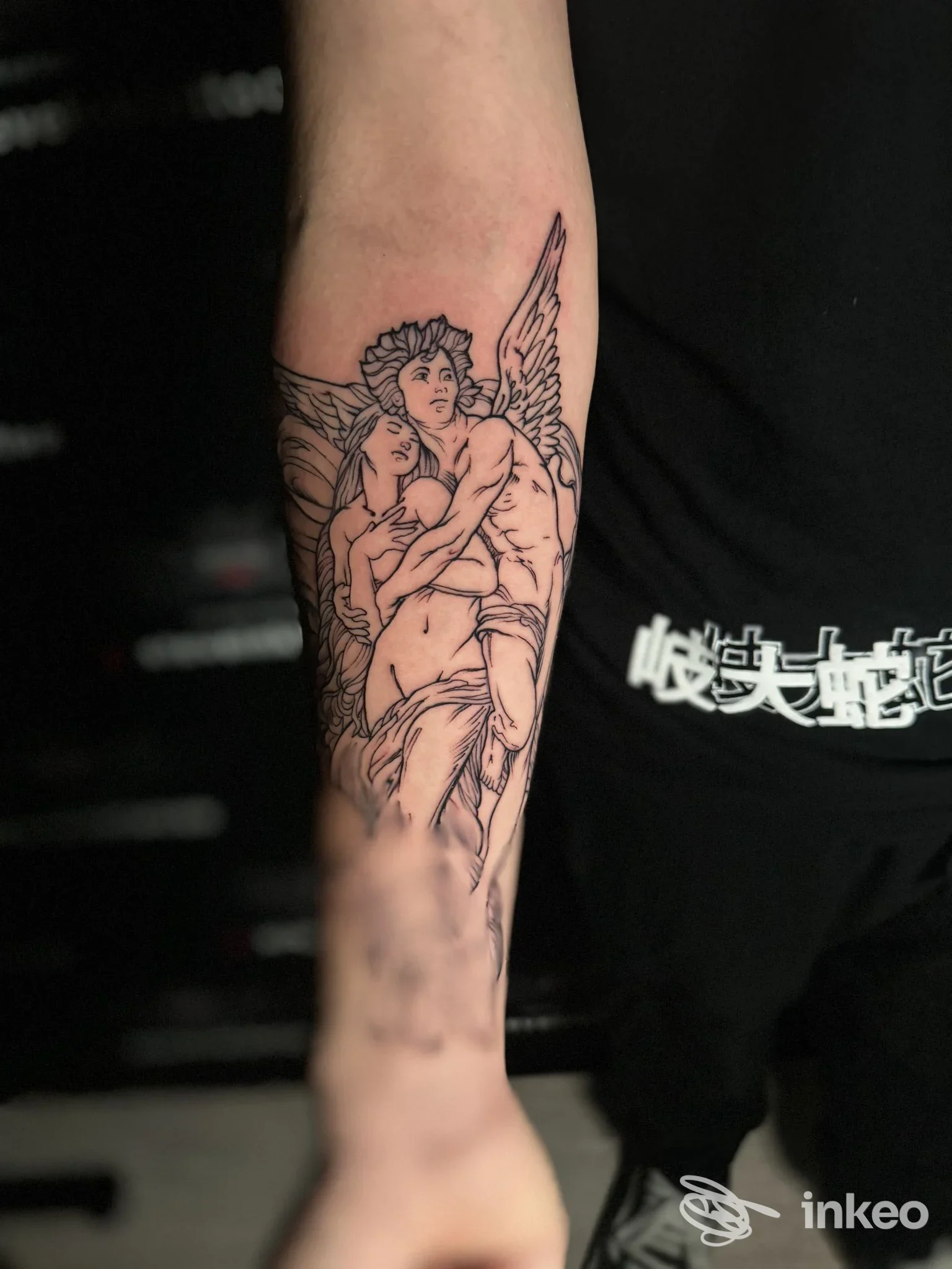 Tattoo raffigurante due figure angeliche abbracciate lungo l'avambraccio, eseguito sul braccio sinistro, stile linework, senza testo visibile.