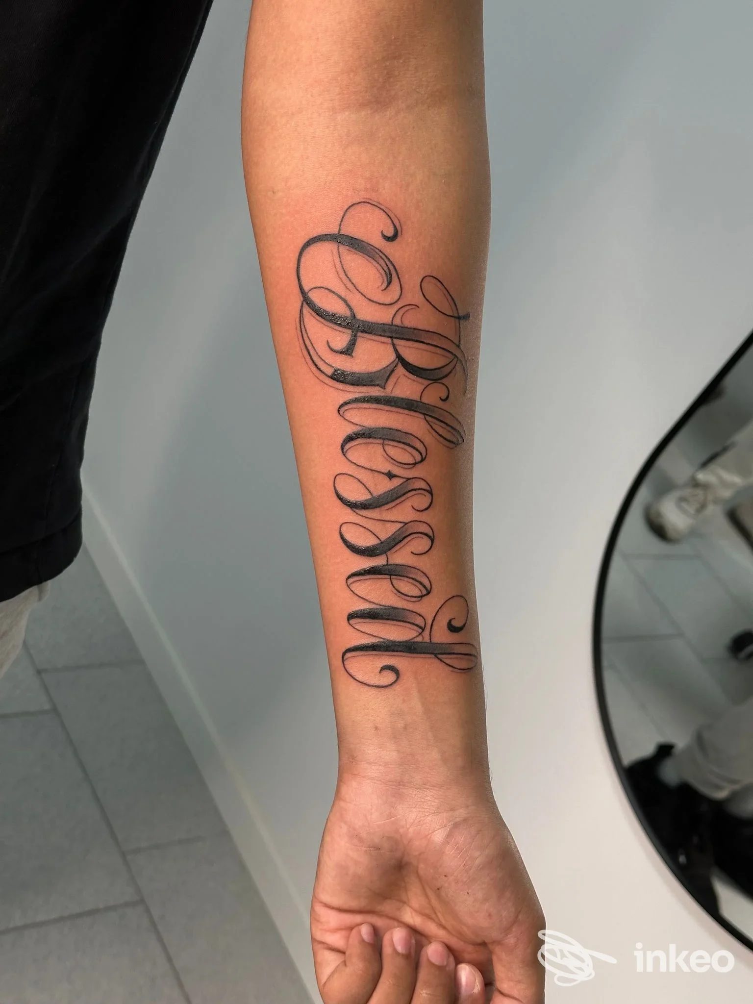 Tattoo originale visibile sull’avambraccio con stile calligrafico verticale, inchiostro nero definito e contorni puliti.
