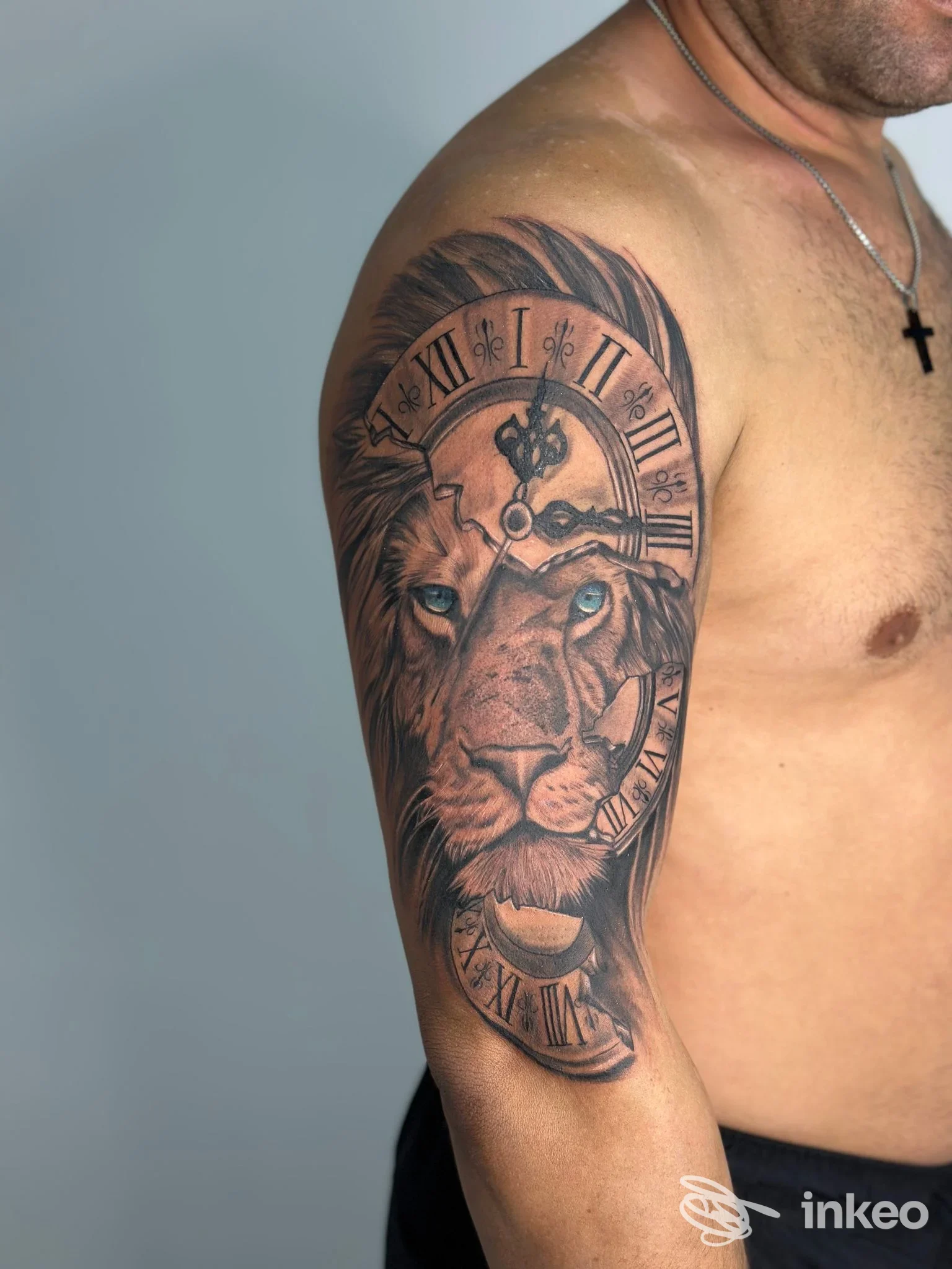 Tatuaggio realistico sul braccio sinistro: una testa di leone con un orologio roman numeralico intorno, in bianco e nero, tatuato sulla pelle nuda.