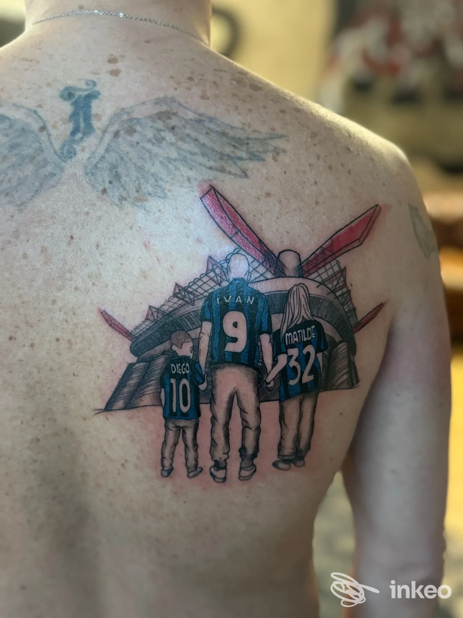 Tattoo visibile sulla schiena raffigurante quattro persone viste di spalle con maglie numerate e sfondo decorativo, realizzazione corporea chiara.
