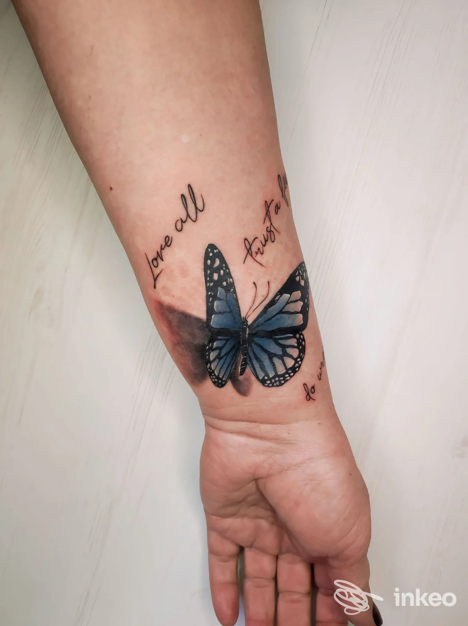 Tattoo reale su avambraccio raffigurante una farfalla blu con scritte attorno.