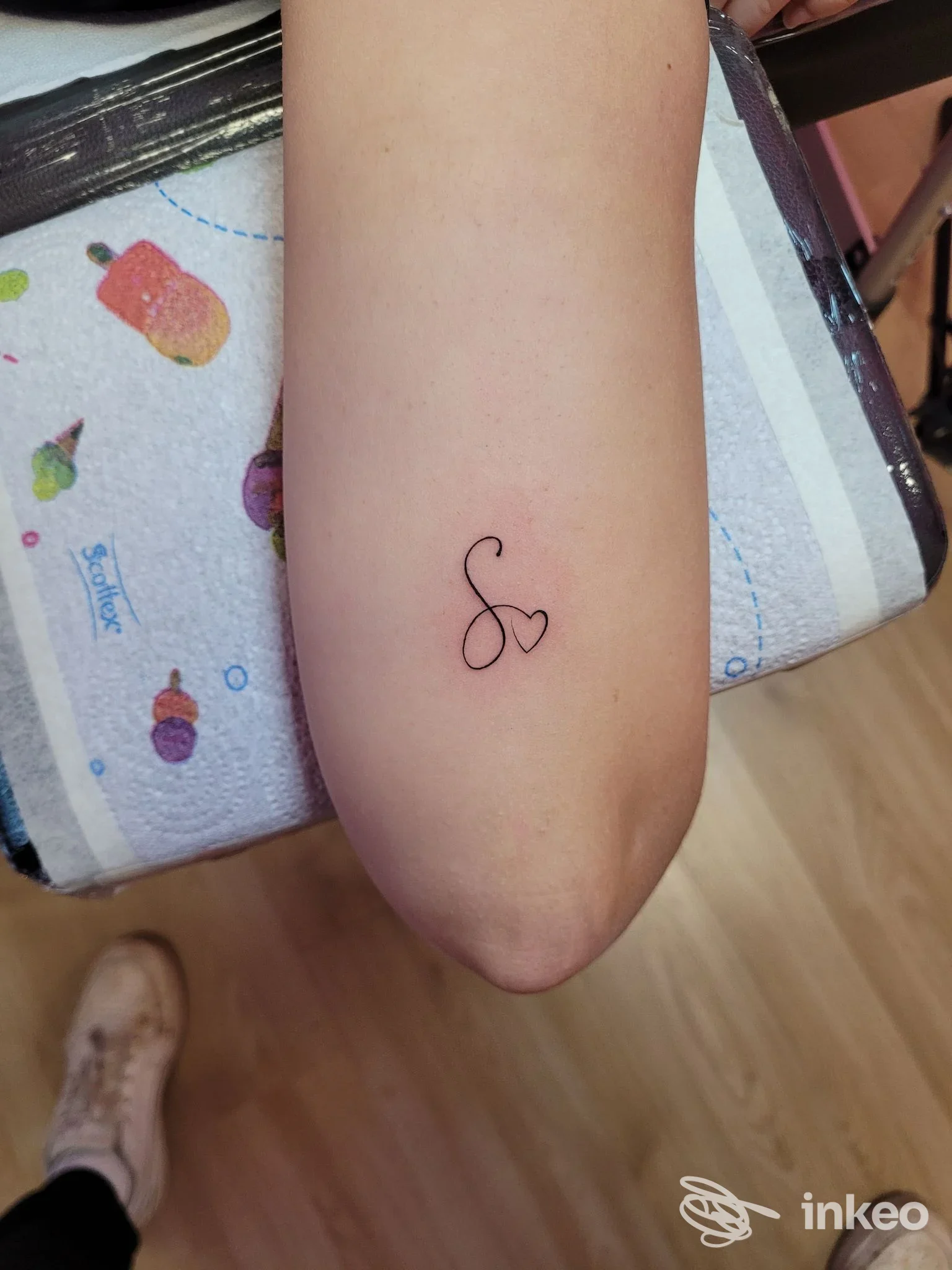 Piccolo tatuaggio sul braccio raffigurante una S stilizzata con un cuore, eseguito da Kame House tattoo shop.