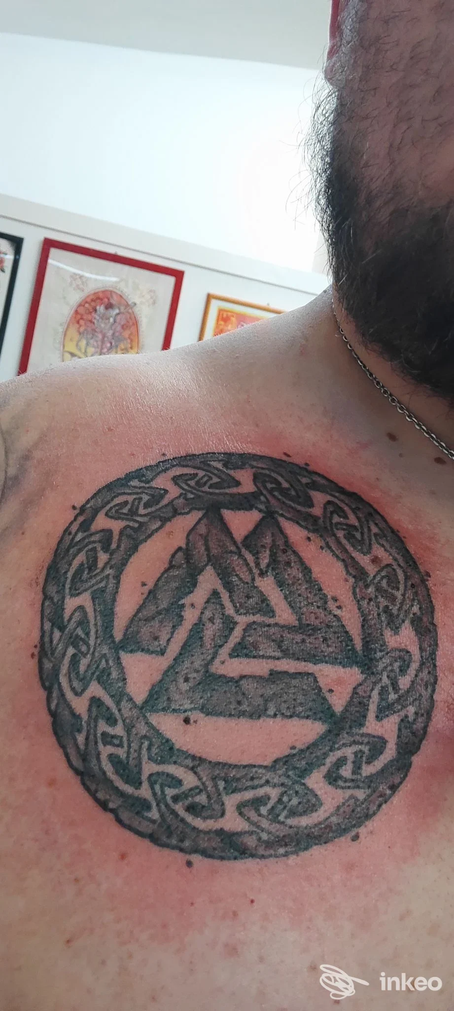 Tattoo circolare in stile blackwork sul torace sinistro con motivo intrecciato e triangoli interni, contorno a catena, visibile su pelle.