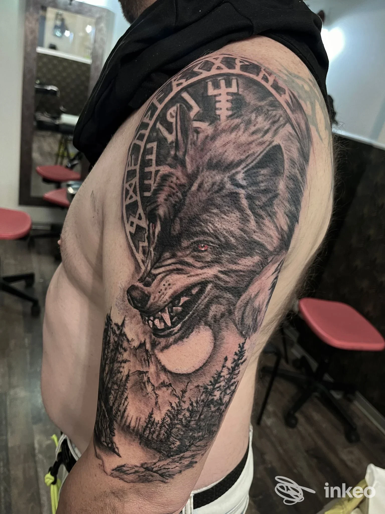 Tattoo realistico di lupo su braccio, in bianco e nero, con cornice circolare e sfondo scuro, scatto laterale in studio Semantika Tattoo.