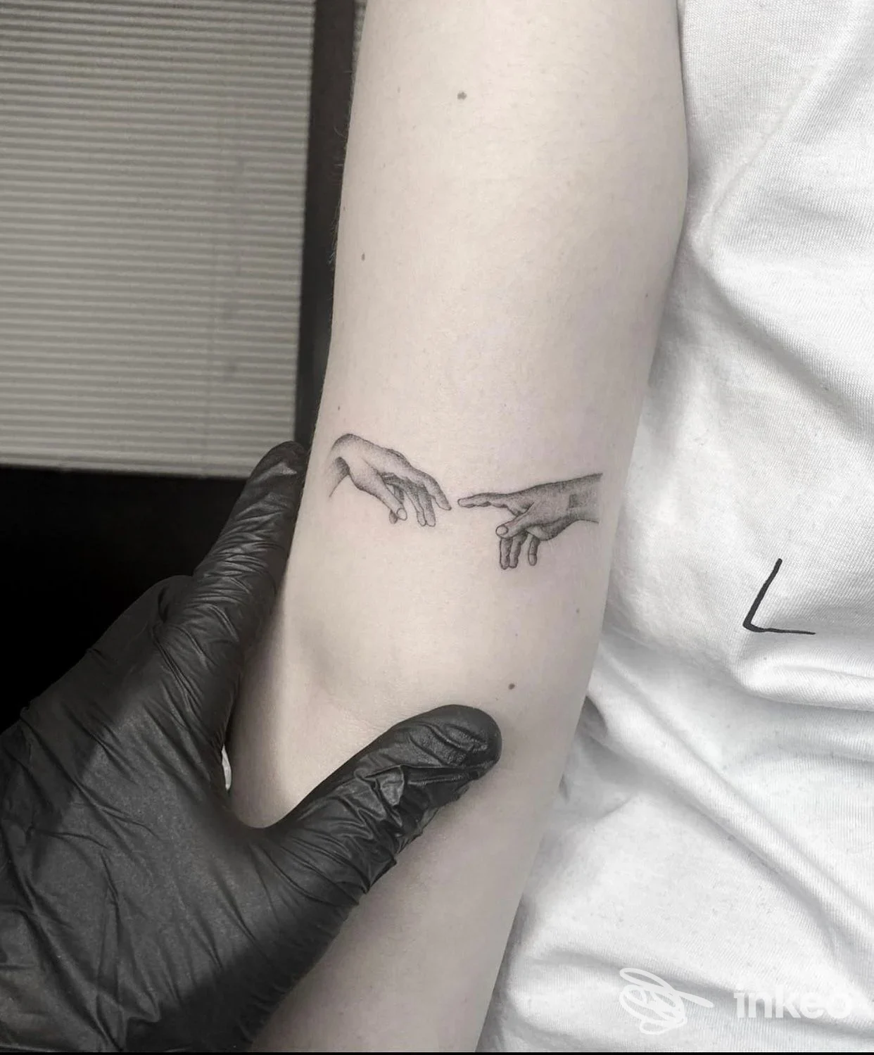 Tatuaggio raffigurante due mani che si sfiorano sull’avambraccio di una persona, realizzato sulla pelle; scatto frontale. Studio Loris Tattoo.