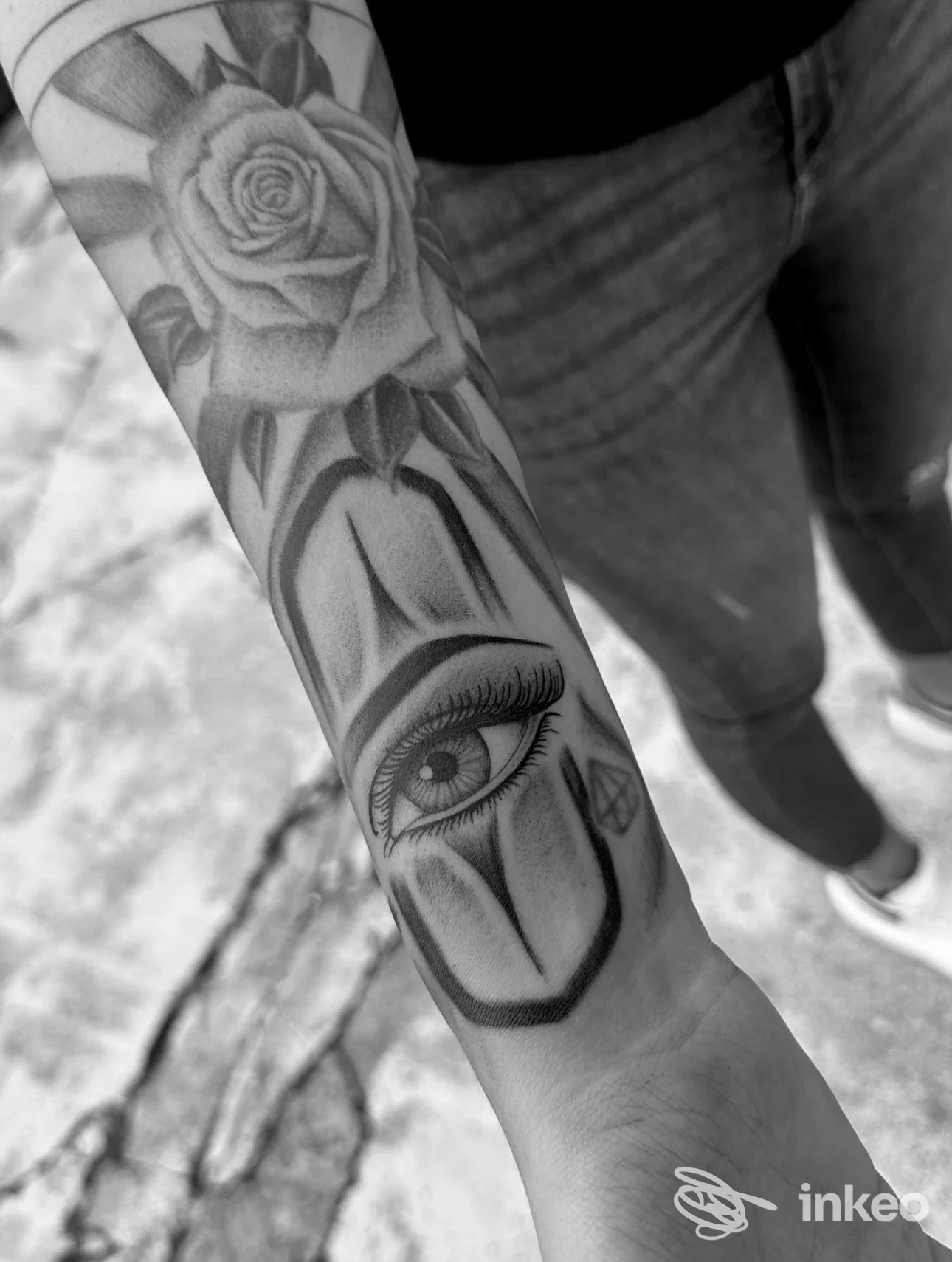 Fotografia in bianco e nero di un avambraccio con tatuaggio: rosa dettagliata lungo la pelle e motivo geometrico, senza viso né elementi promozionali visibili. Studio Loris Tattoo, località non indicata.