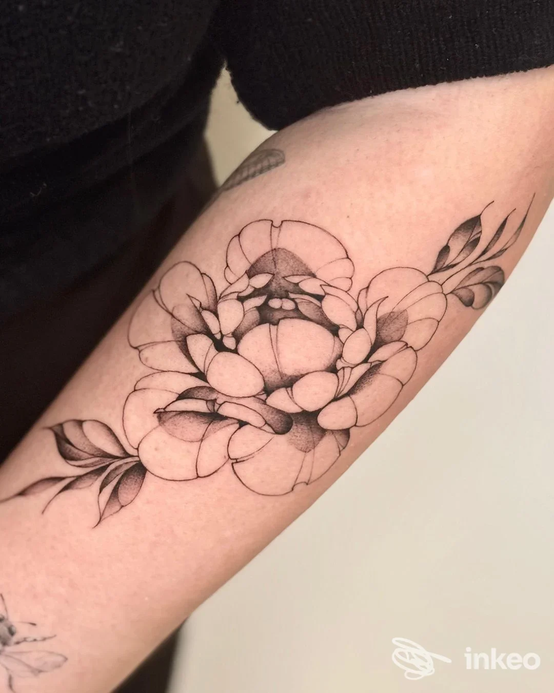 Tattoo floreale in toni neri sull’avambraccio, eseguito sulla pelle, con linee pulite e sfumature leggere senza contenuti aggiuntivi.