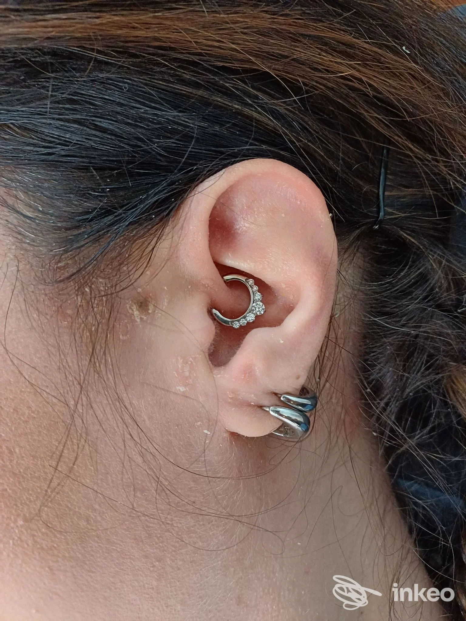 Piercing all'orecchio con mezzaluna incastonata di pietre e due anelli sul lobo, visibile sul orecchio di una persona; studio Snakesstudio.