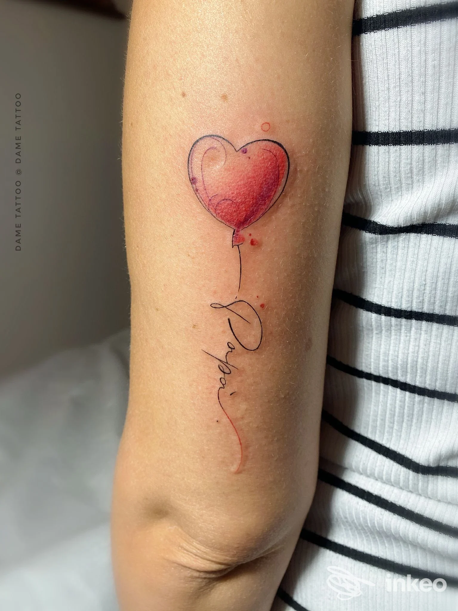 Tattoo visibile sull’avambraccio: un palloncino a cuore rosso con la stringa decorativa. grafica sottile e dettagliata, nessun volto visibile, nessuna sovraimpressione di social.