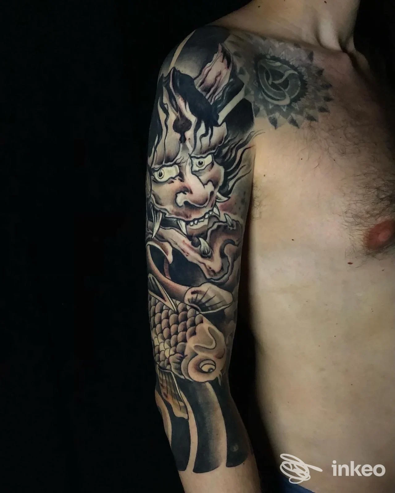 Braccio sinistro con tattoo a tema giapponese, figura demoniaca e motivi d'acqua, su pelle reale, sfondo nero