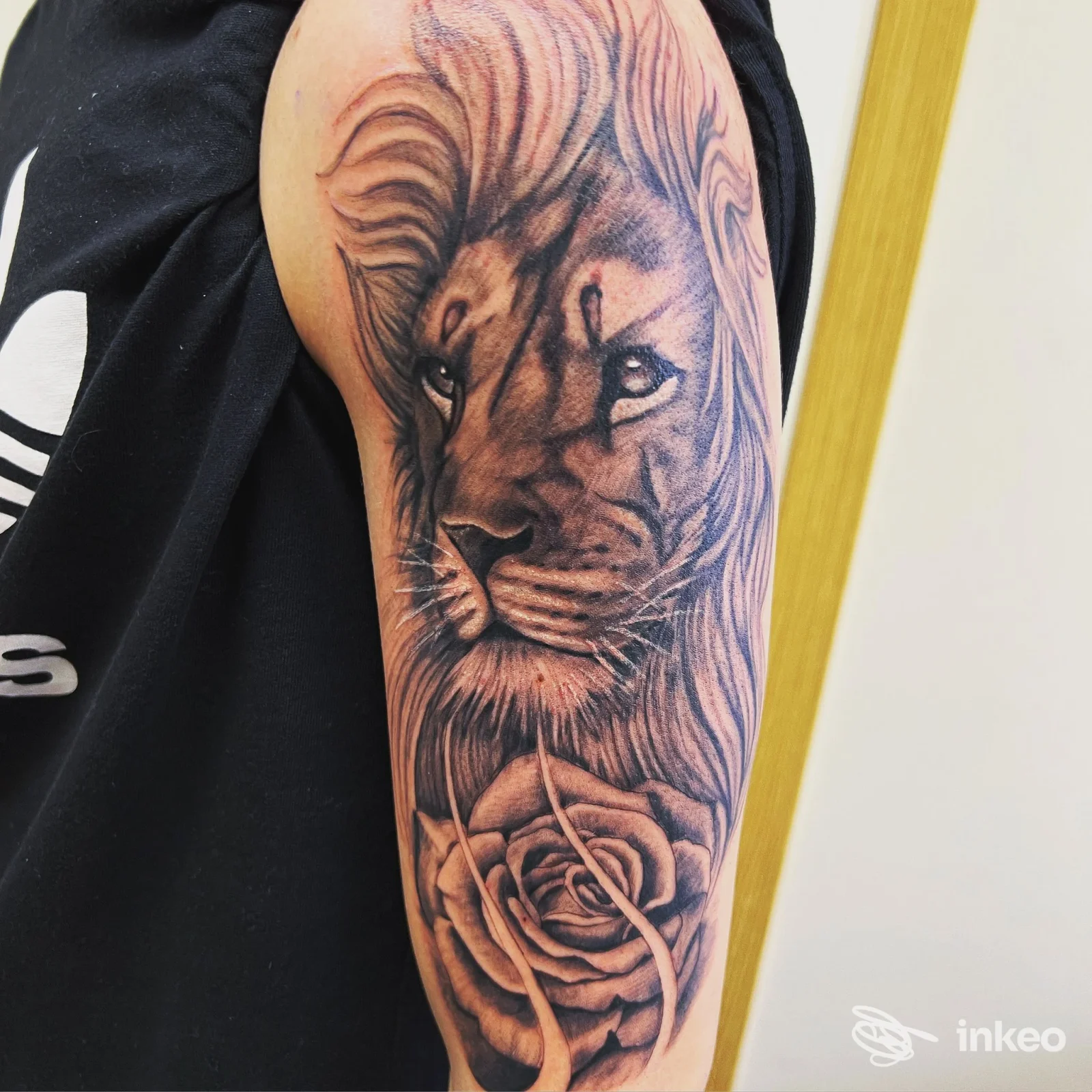 Tattoo realistico di leone sul braccio con rosa, realizzato su pelle, in bianco e nero, visibile da vicino.