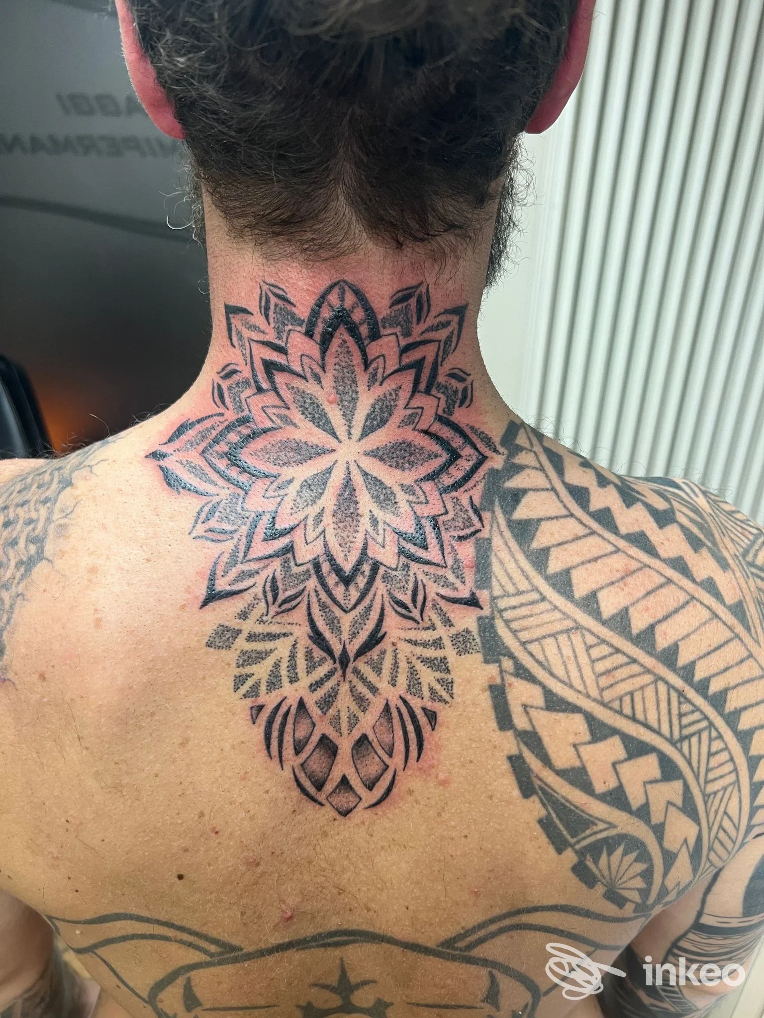 Tattoo geometrico a mandala sulla nuca e sulla parte alta della schiena, tatuaggio visibile su pelle reale senza volto, con altre incisioni sul lato destro della schiena.