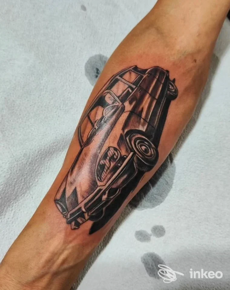 Tatuaggio realistico su avambraccio raffigurante un veicolo; tatuaggio nero-grigio su pelle, nessun volto visibile, nessun overlay, inquadratura singola.