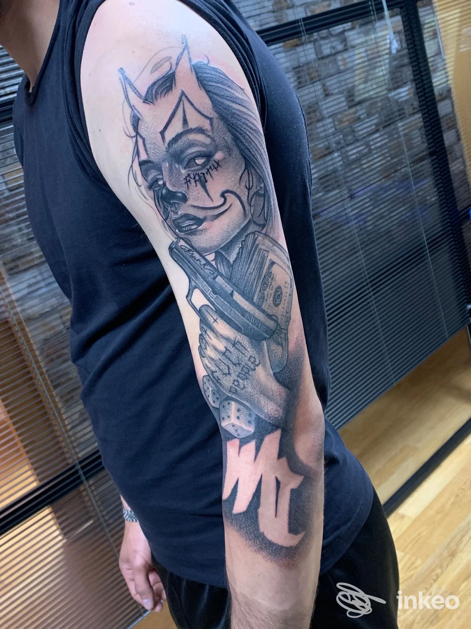 Tattoo sul braccio di una persona, disegno in stile grafico, lucido in bianco e nero, visibile lungo avambraccio e parte superiore; lo sfondo è un ambiente di studio.