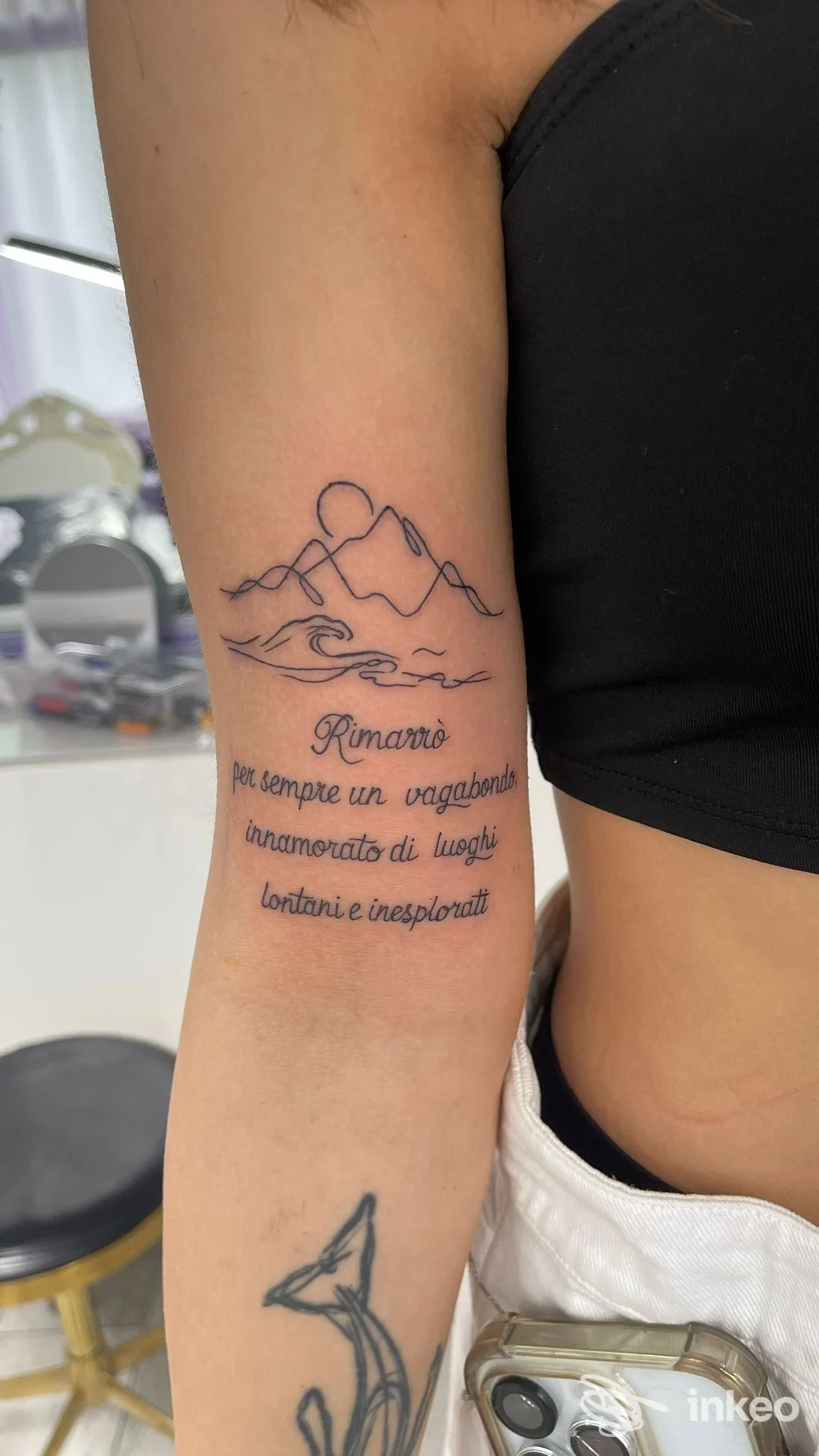 Tatuaggio visibile sull’avambraccio: montagna stilizzata con testo corsivo sotto, realizzato sulla pelle, senza overlay o testo promozionale.