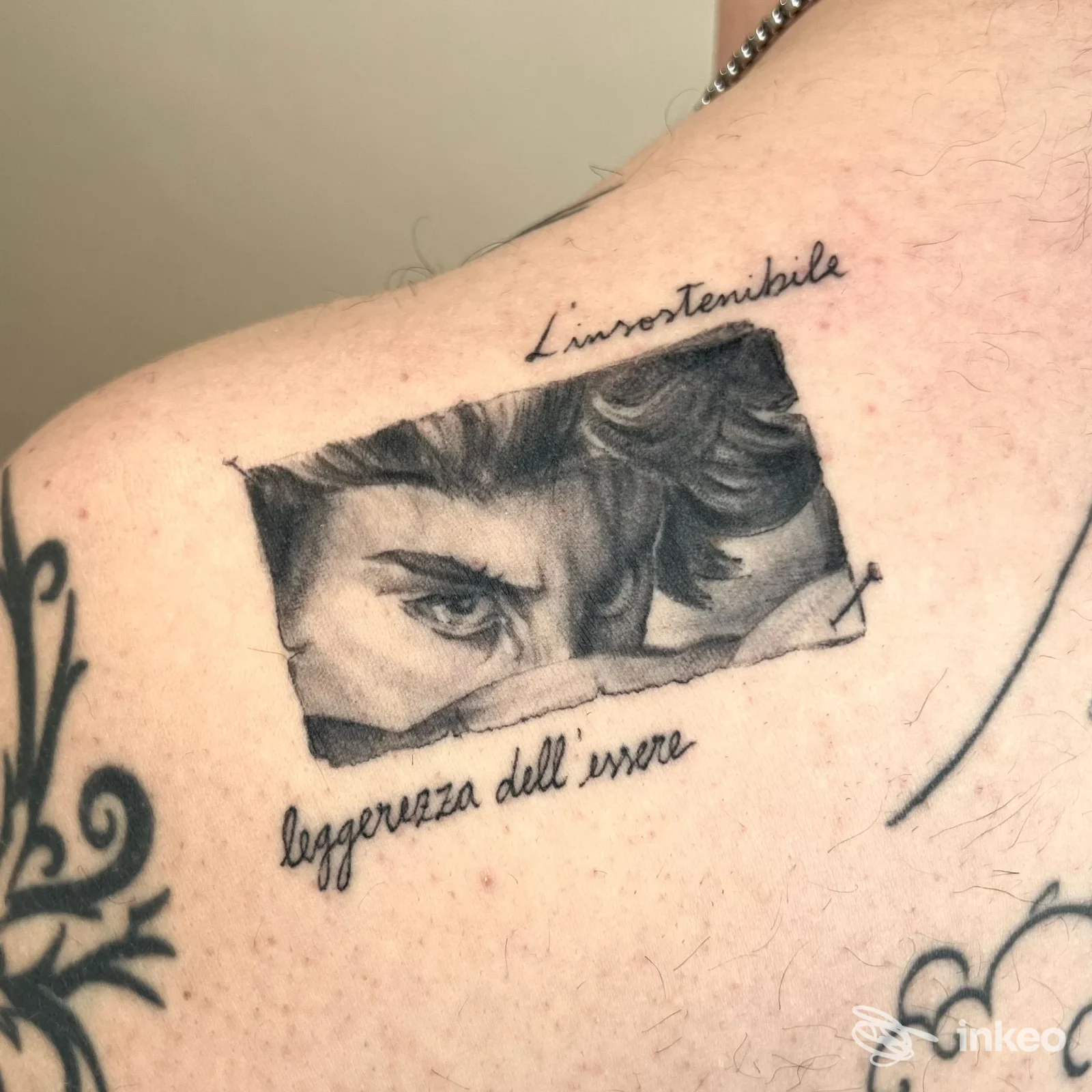 Tatuaggio realistico sull'avambraccio/spalla: un occhio parzialmente visibile emerge da una feritoia di carta o taglio, accompagnato da didascalie corsive. sul tessuto si legge probabilmente una citazione.