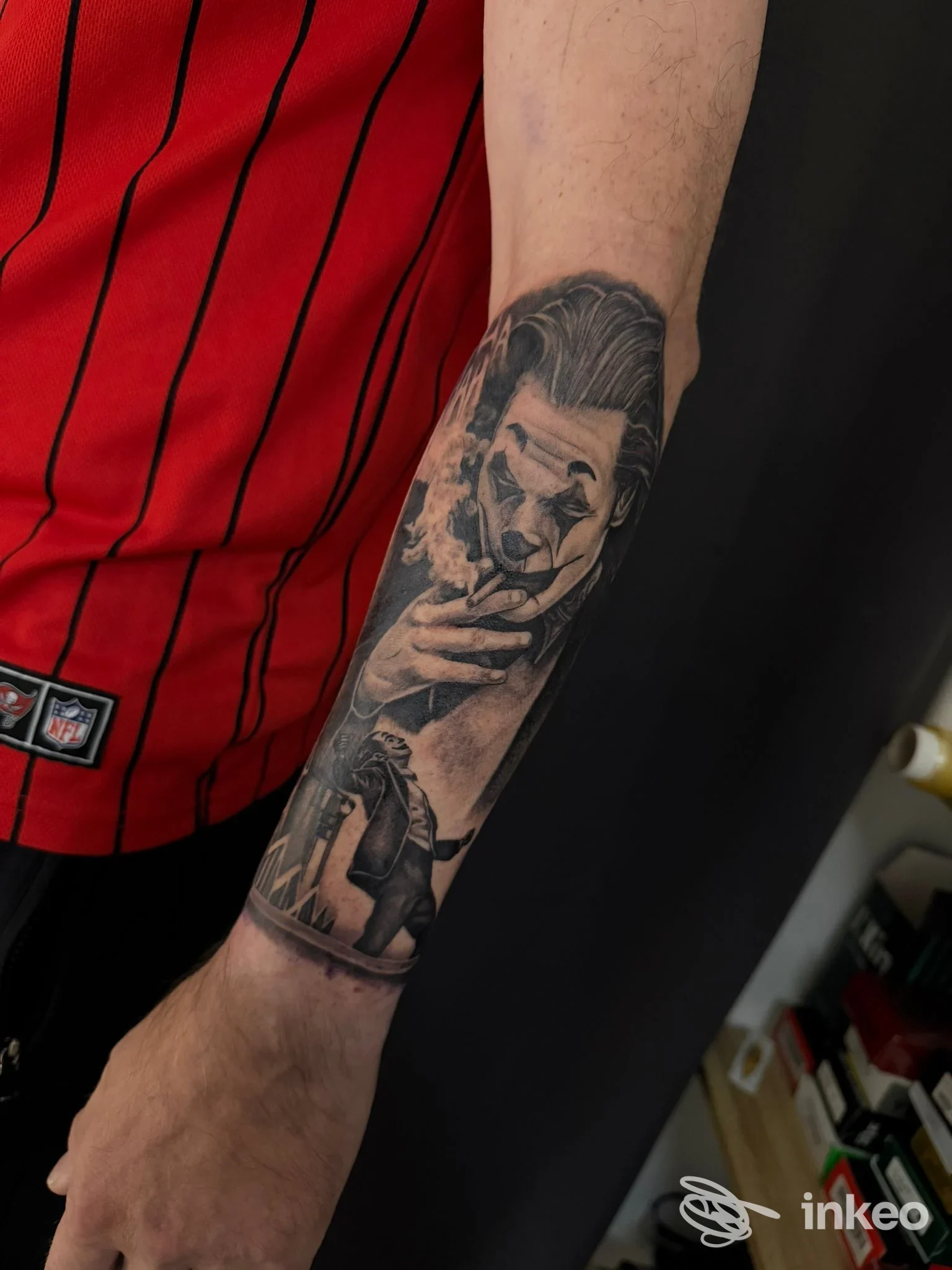 Immagine di sotto-lancio del braccio di una persona con tatuaggio realistico al polso e avambraccio, su sfondo scuro, indossa una maglia rossa a righe nere.