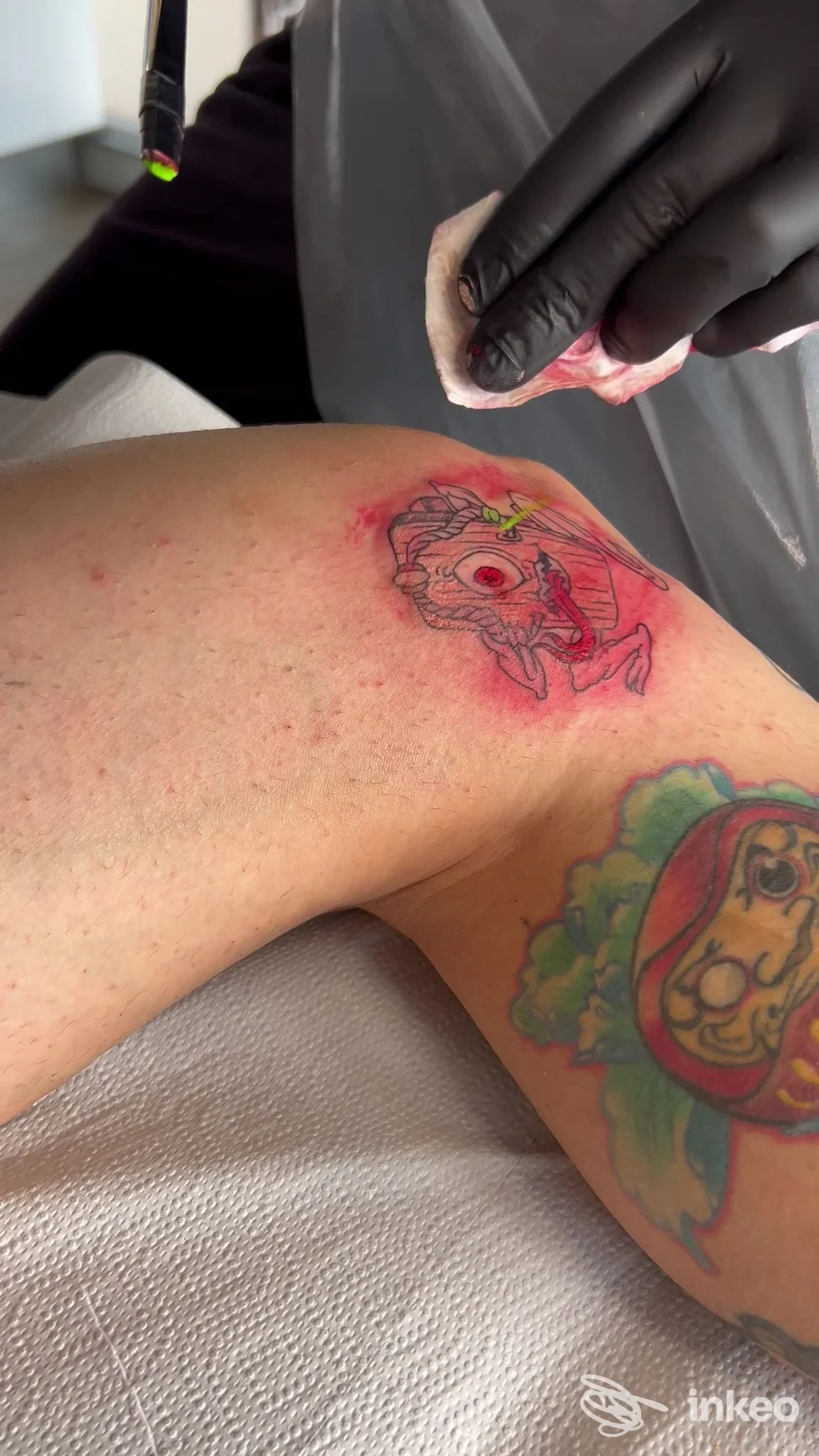 Veduta laterale di una gamba con tatuaggi colorati, tra cui un disegno rosso contornato e un motivo multicolore visibile sulla pelle.