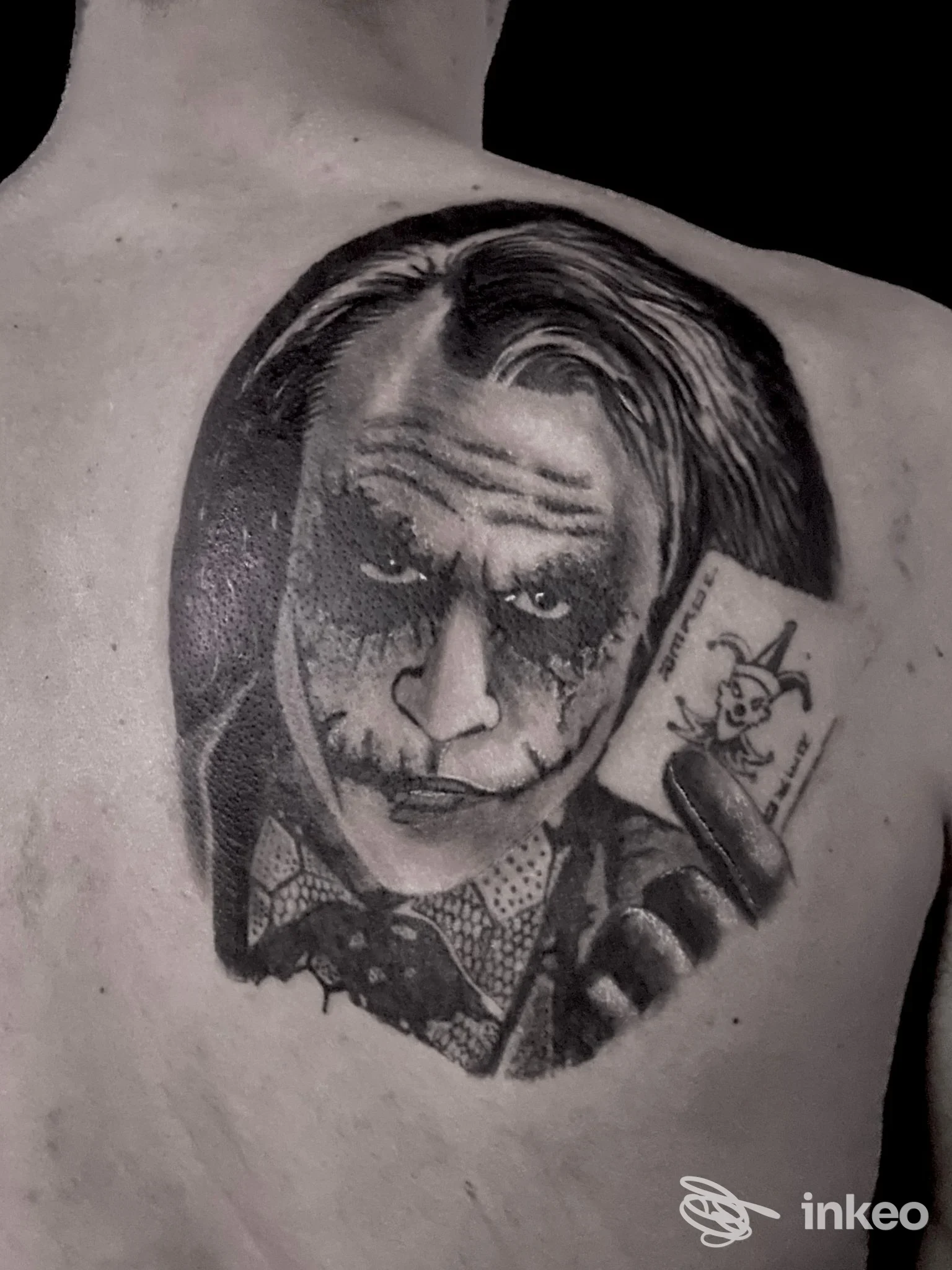 Tattoo realistico in bianco e nero sul dorso di una persona, raffigurante il Joker, visibile sulla spalla sinistra.