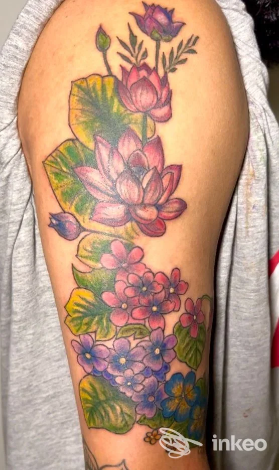 Tatuaggio floreale colorato lungo il braccio su pelle reale, con composizione di lotus e altri fiori.