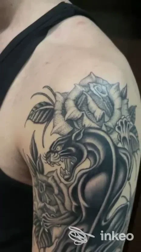 Tattoo visibile su braccio superiore, raffigurante un drago scuro con rose adiacenti, eseguito su pelle reale, nessun testo o overlay visibile.