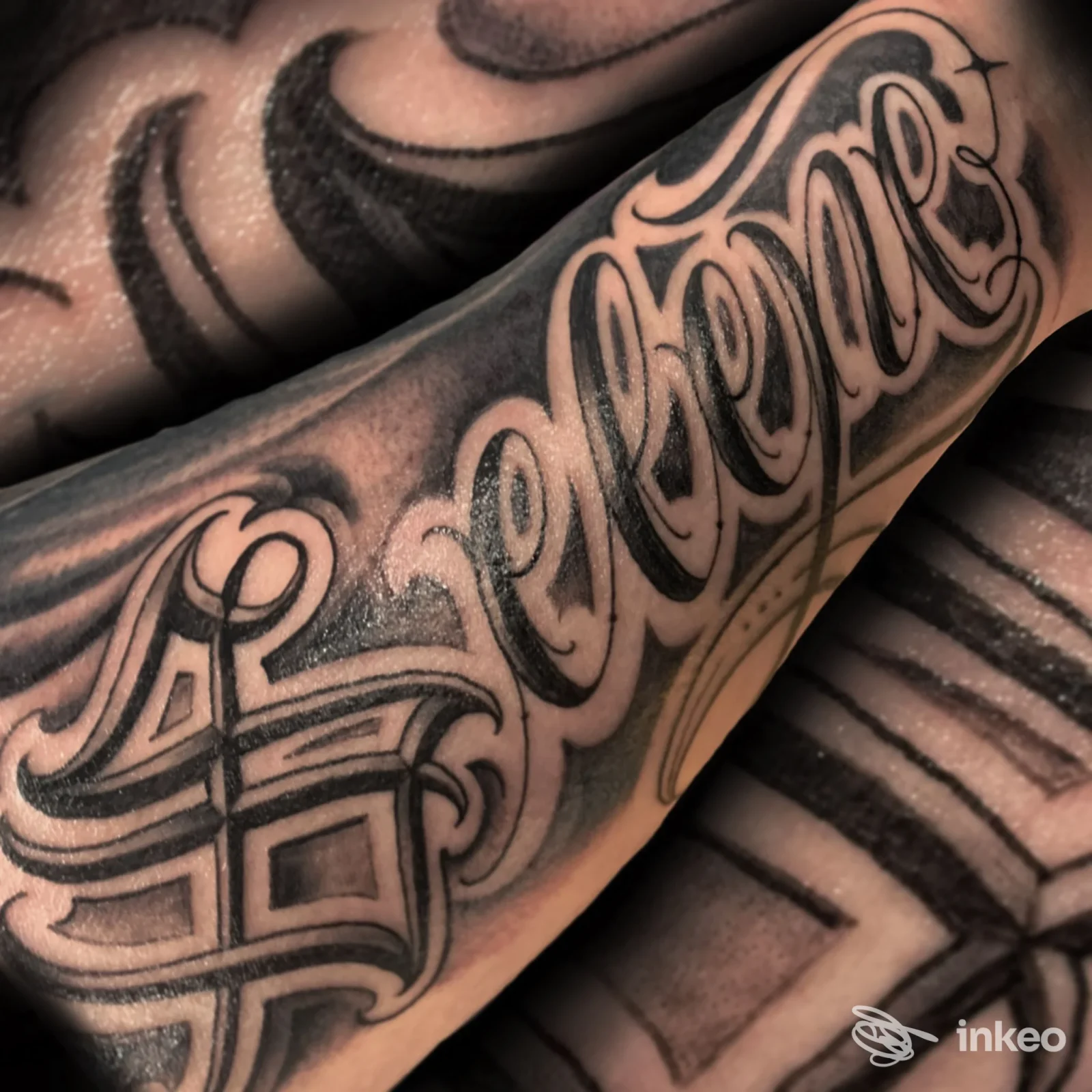 Tattoo script sul braccio, contorni scuri e riempimento nero, visibile su pelle reale senza volto mostrado, realizzato da studio non indicato.