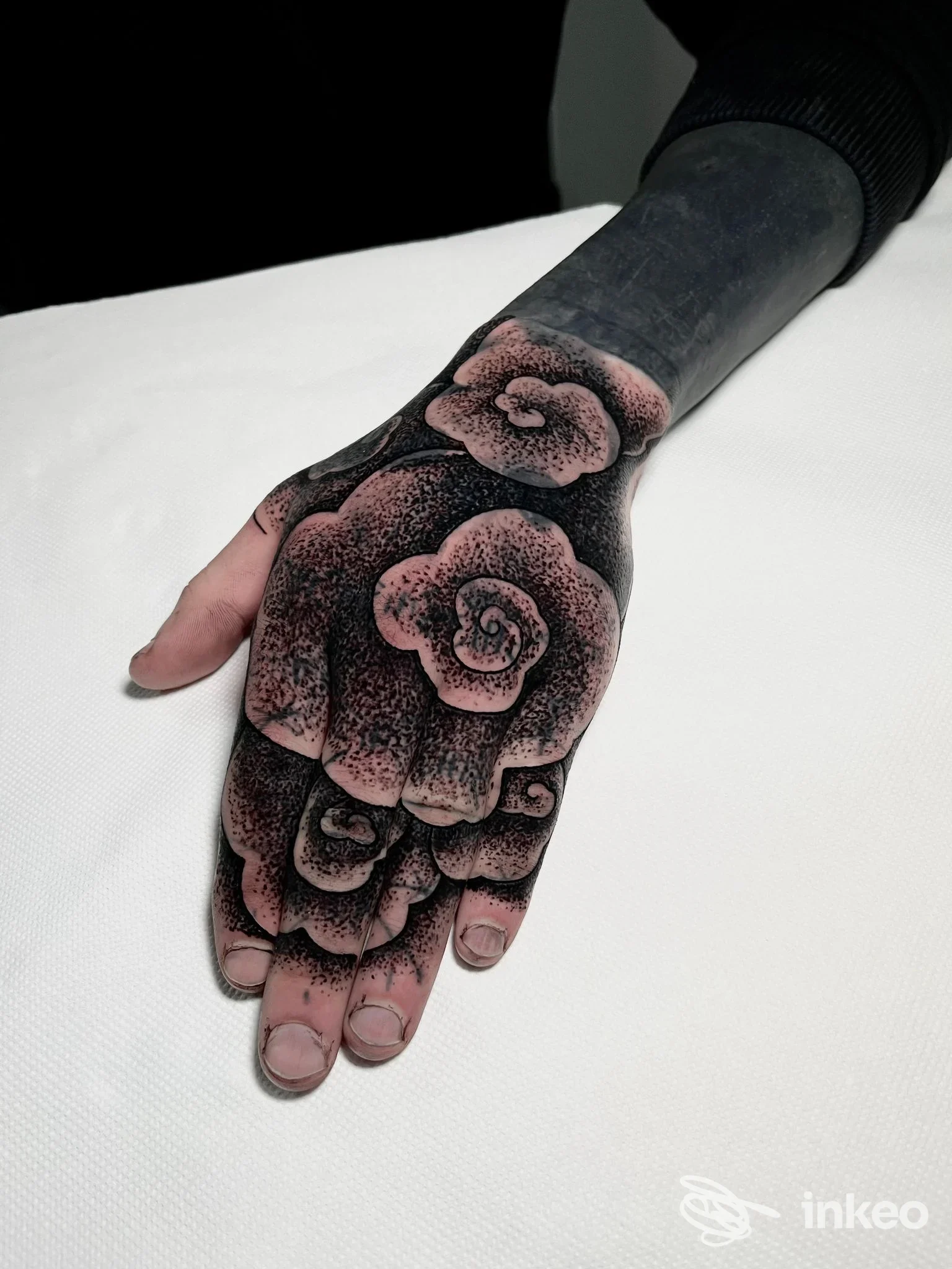 Tatuaggio su dorso della mano raffigurante rose rosa su sfondo scuro, con dettagli e sfumature; esposto su superficie bianca.