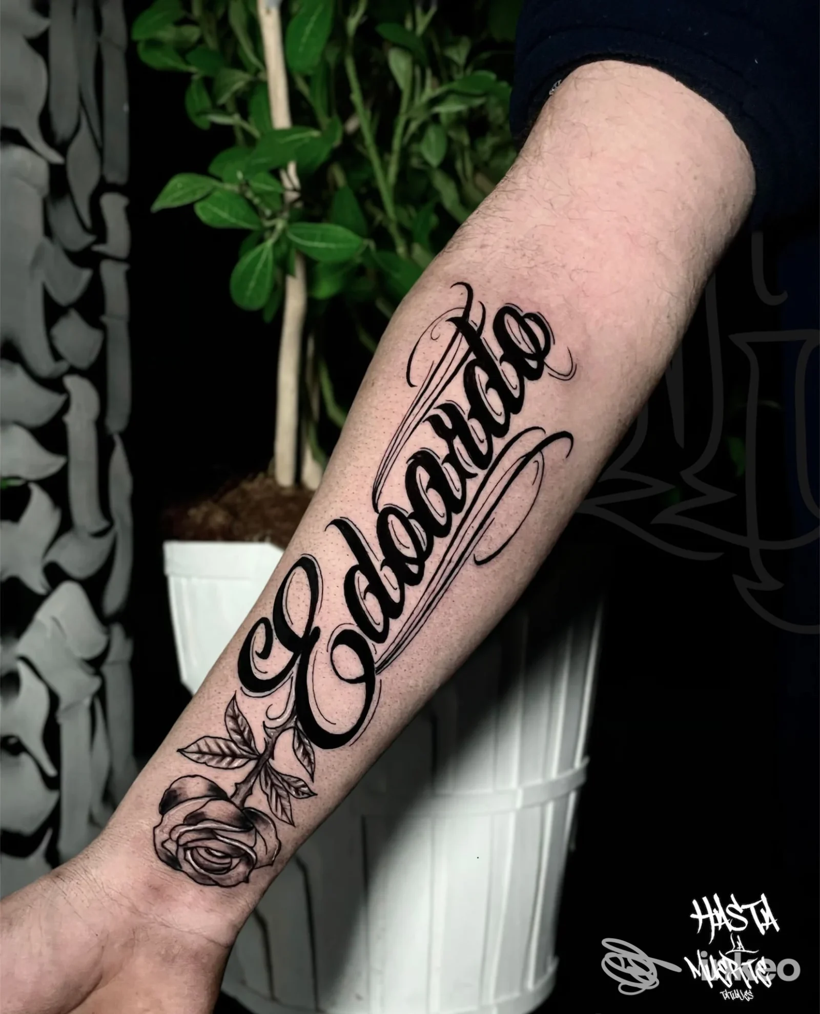 Tattoo sull’avambraccio di una persona: una scritta corsiva nera accompagnata da una rosa, realizzata direttamente sulla pelle.