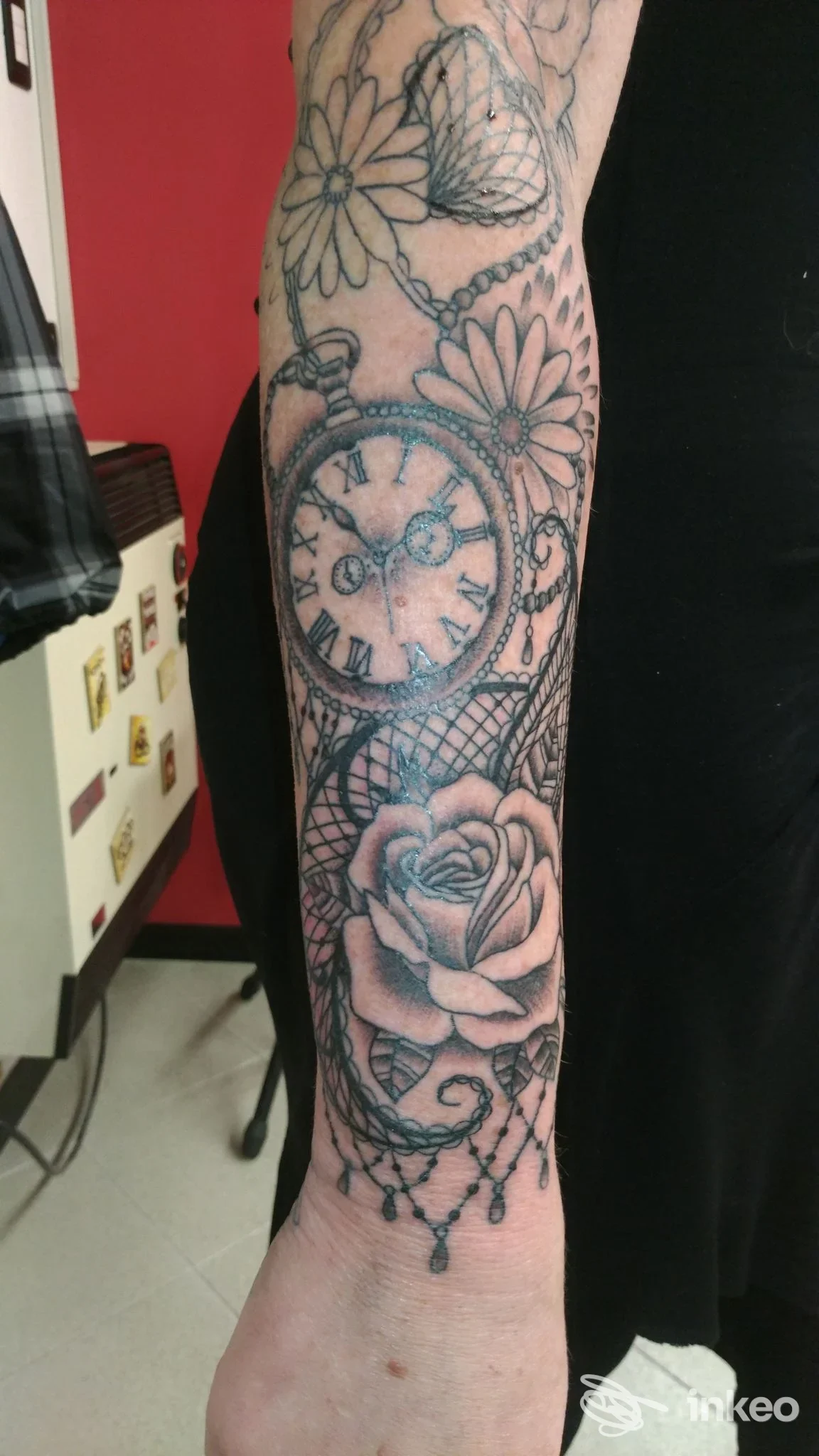 Tatuaggio visibile sul polso con orologio circondato da fiori, realizzato sulla pelle, dettagli nitidi e linee nette.