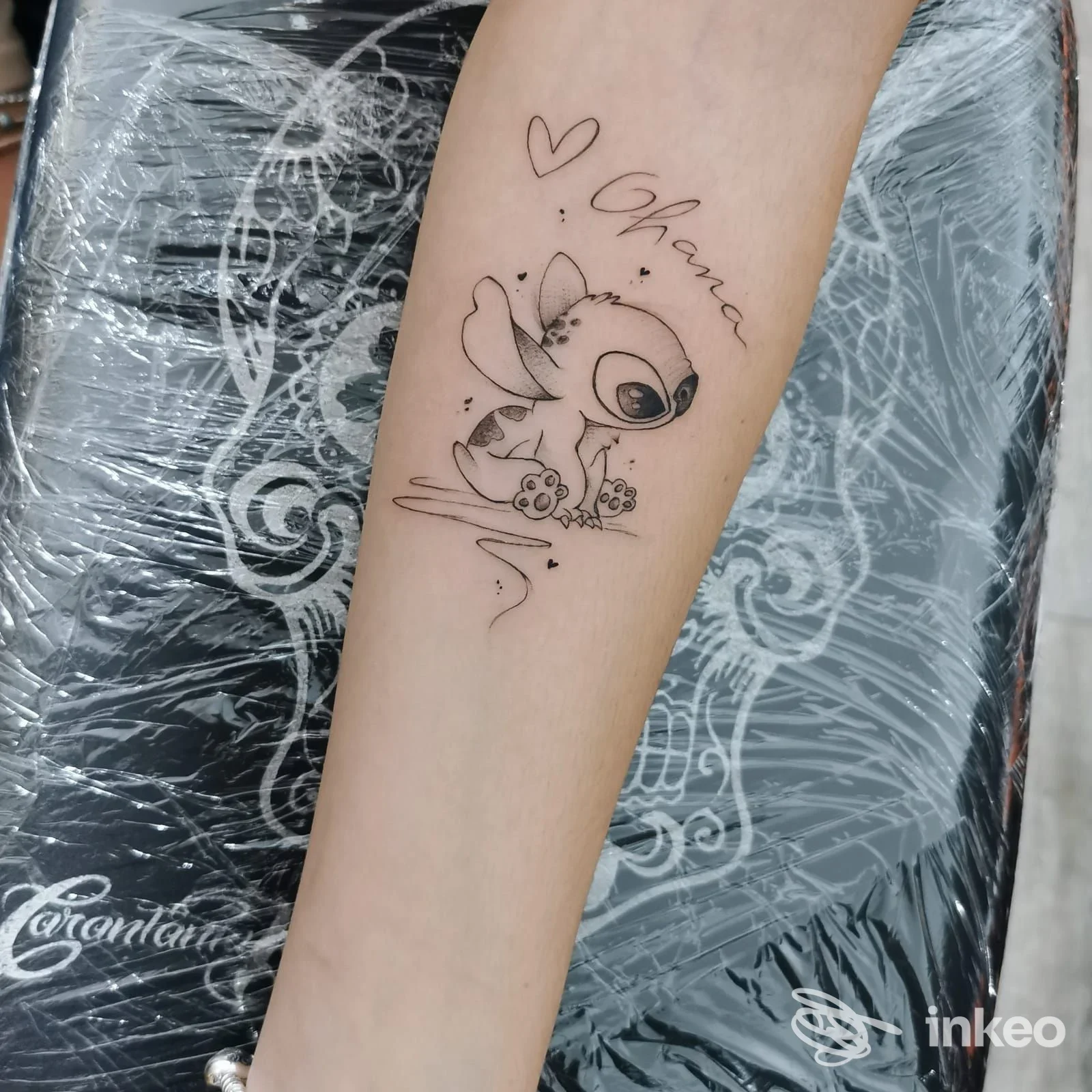 Tattoo piccola su avambraccio sinistro: personaggio cartoon con una piccola figura, scritta a fianco e cuore, scatto singolo a distanza ravvicinata.