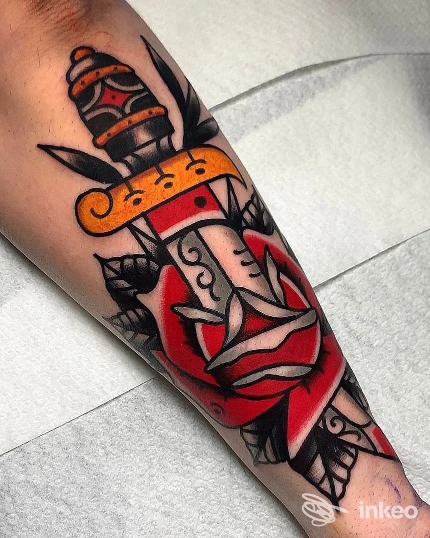 Tattoo su avambraccio raffigurante un pugnale con rosa rossa, colori vivaci e dettagli neri, ottenuto su pelle reale.