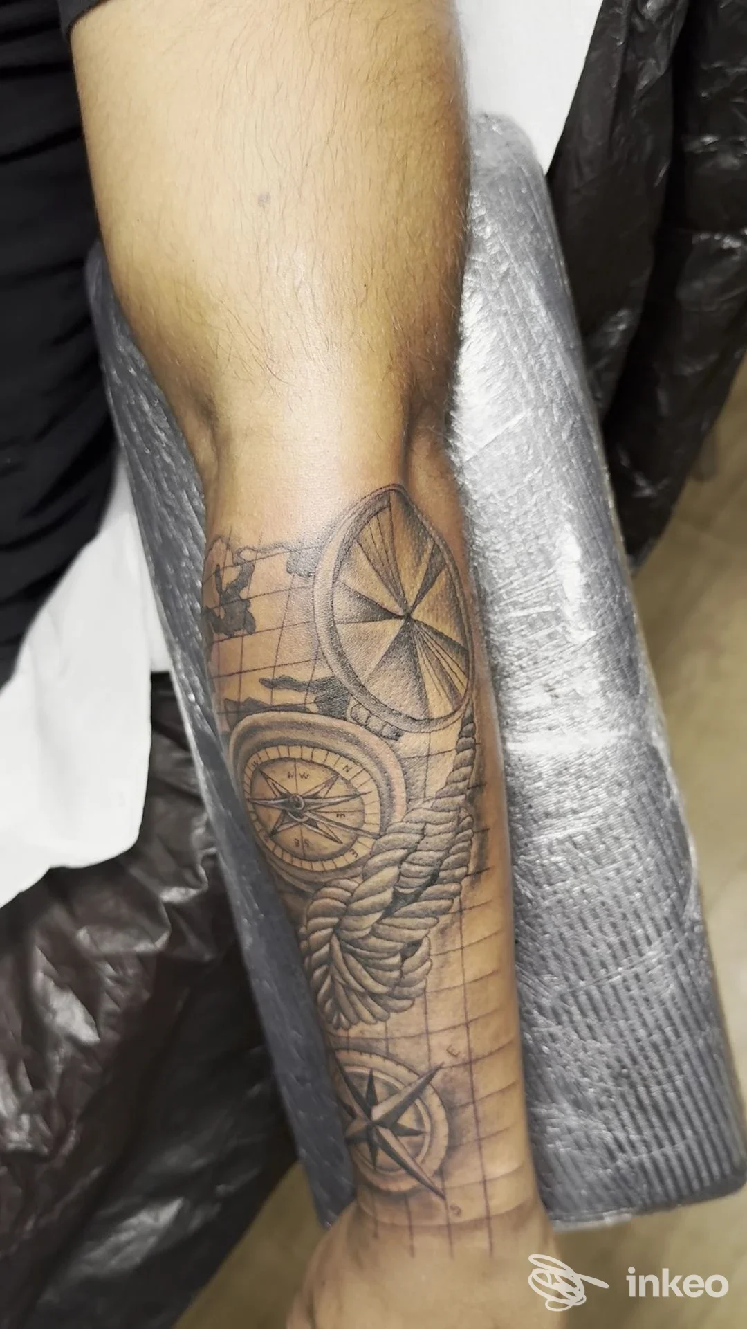 Tattoo sull’avambraccio sinistro raffigurante ruote di carro e corde, visibile su pelle reale in contesto studio; assenza di volto visibile.