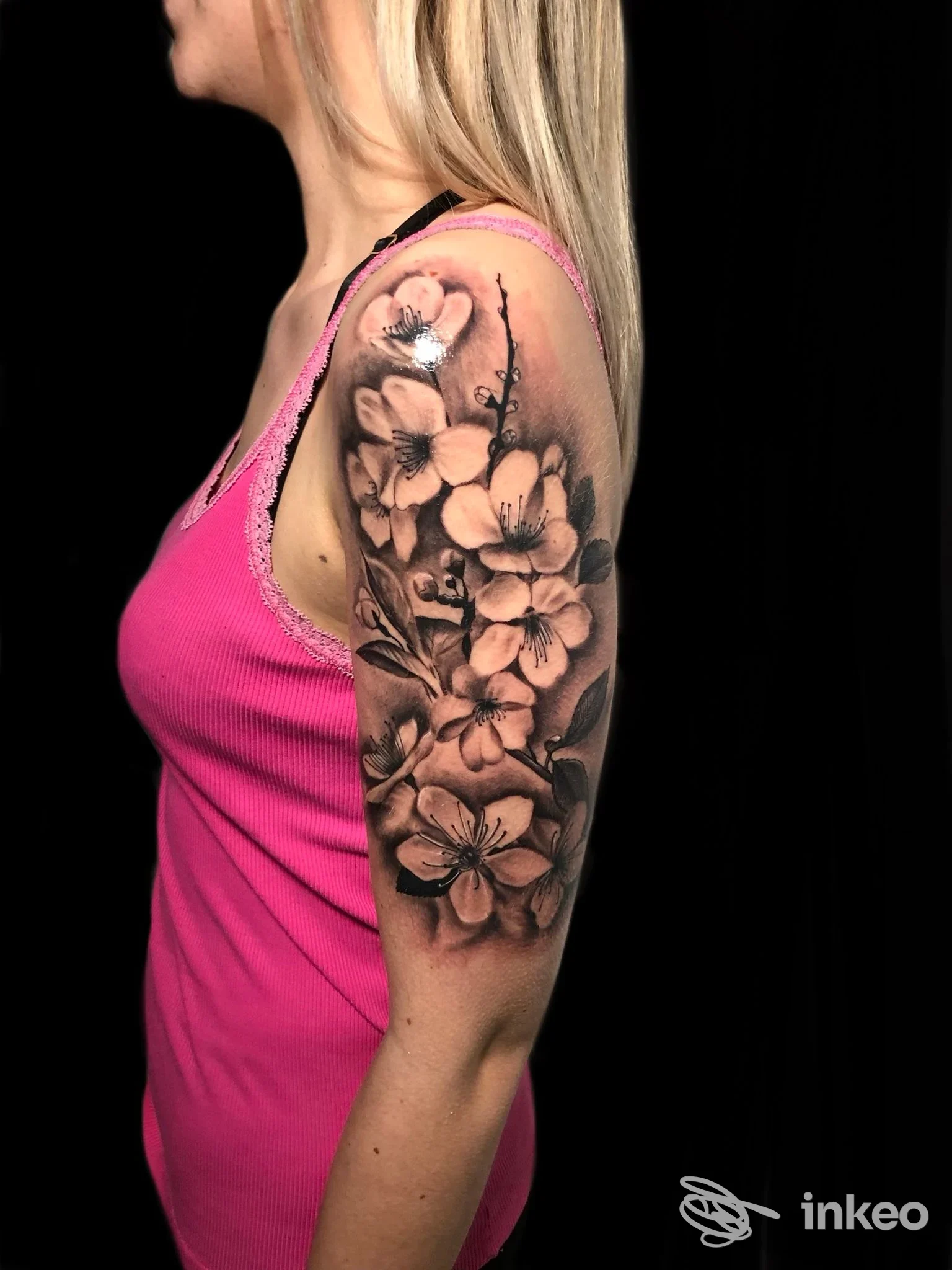 Braccio superiore, tatuaggio realistico di fiori in bianco e nero, sfumature grigie, visibile dalla spalla all’avambraccio, su pelle reale.