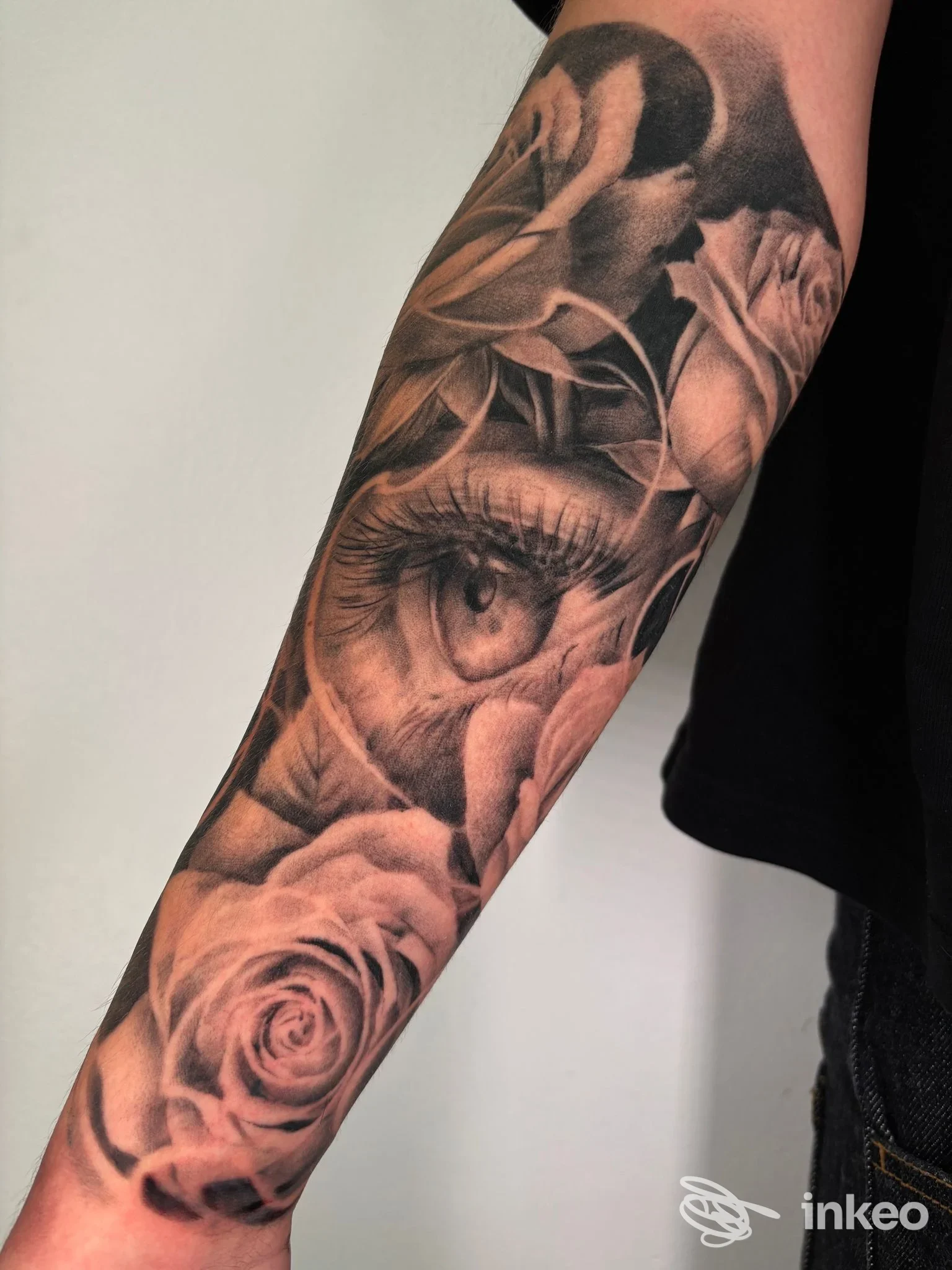 Tattoo in bianco e nero su avambraccio con occhio e rose, scultura di dettagli realistici.