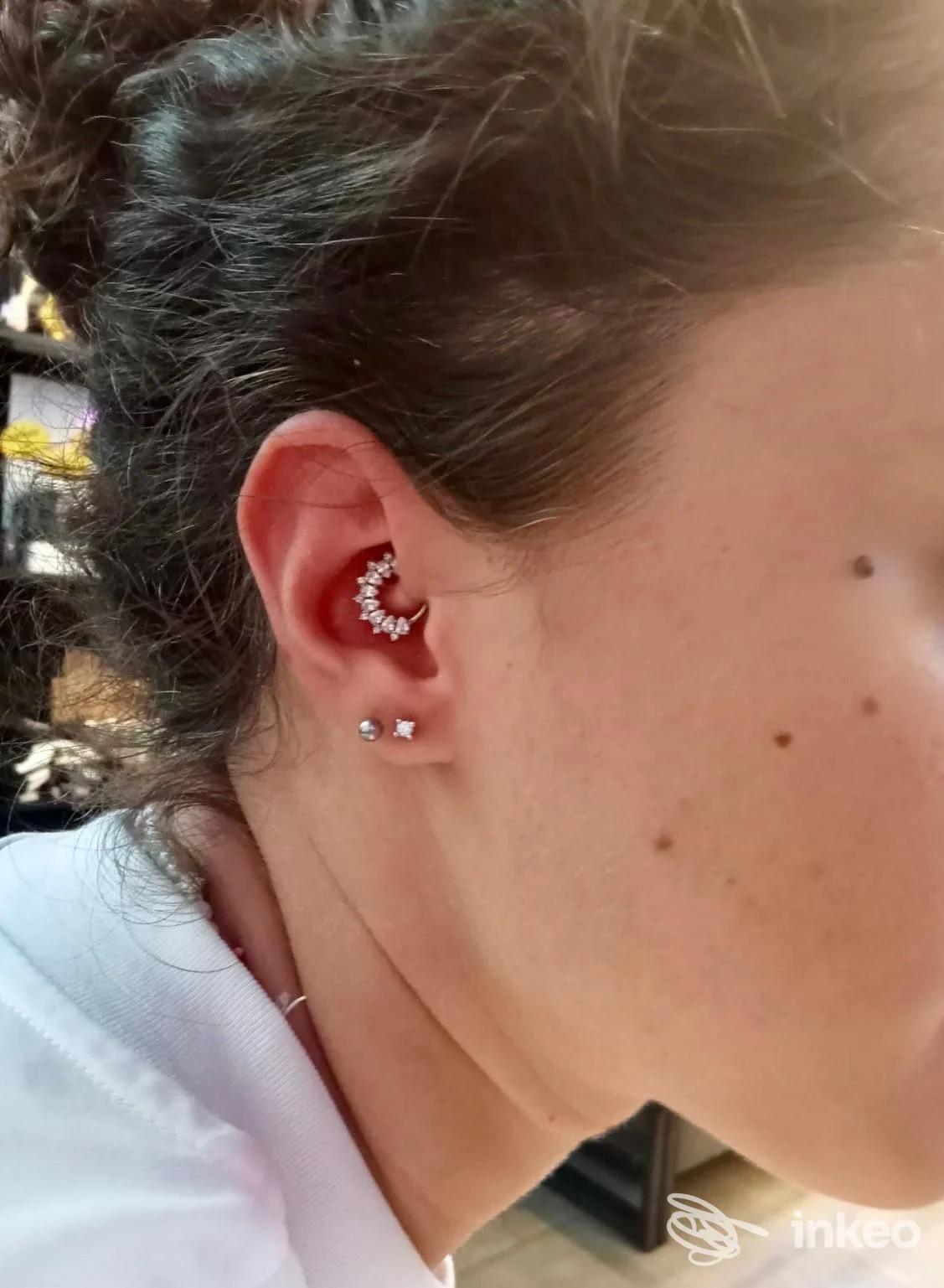 Profilo laterale di una persona con gioielli all’orecchio: un anello curvo sull’elice e due piercing al lobo.