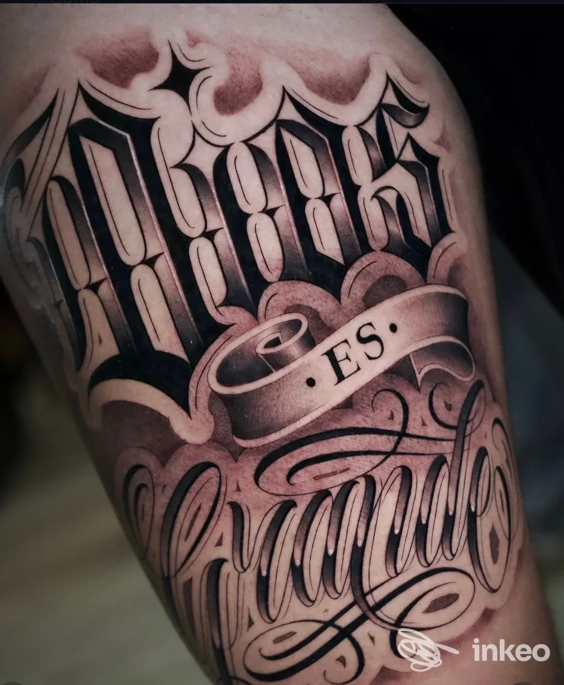 Tattoo sul braccio con lettere in stile gotico e ornamenti, realizzato sulla pelle.