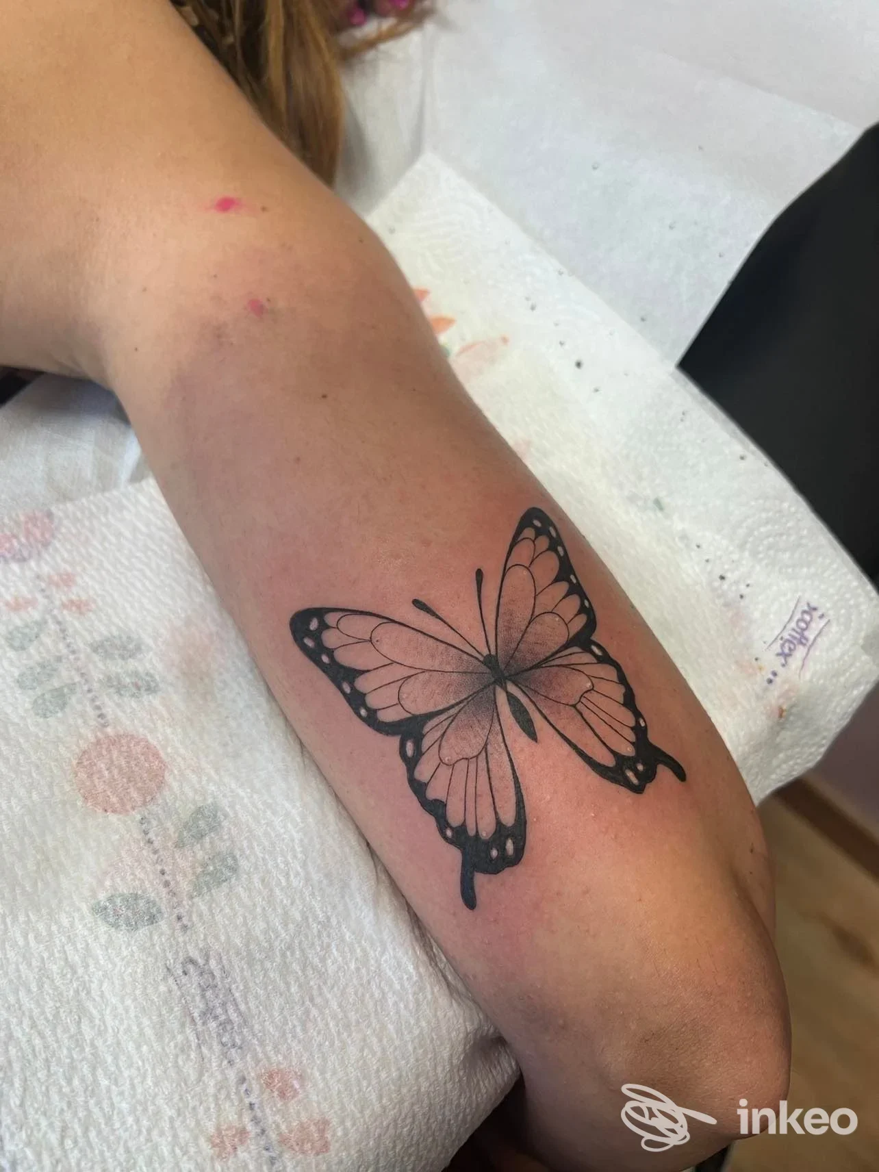 Avambraccio sinistro con tatuaggio a farfalla nera disegnata in stile linework, visibile chiaramente. L'immagine mostra la parte esterna del braccio e la farfalla è l'elemento centrale.