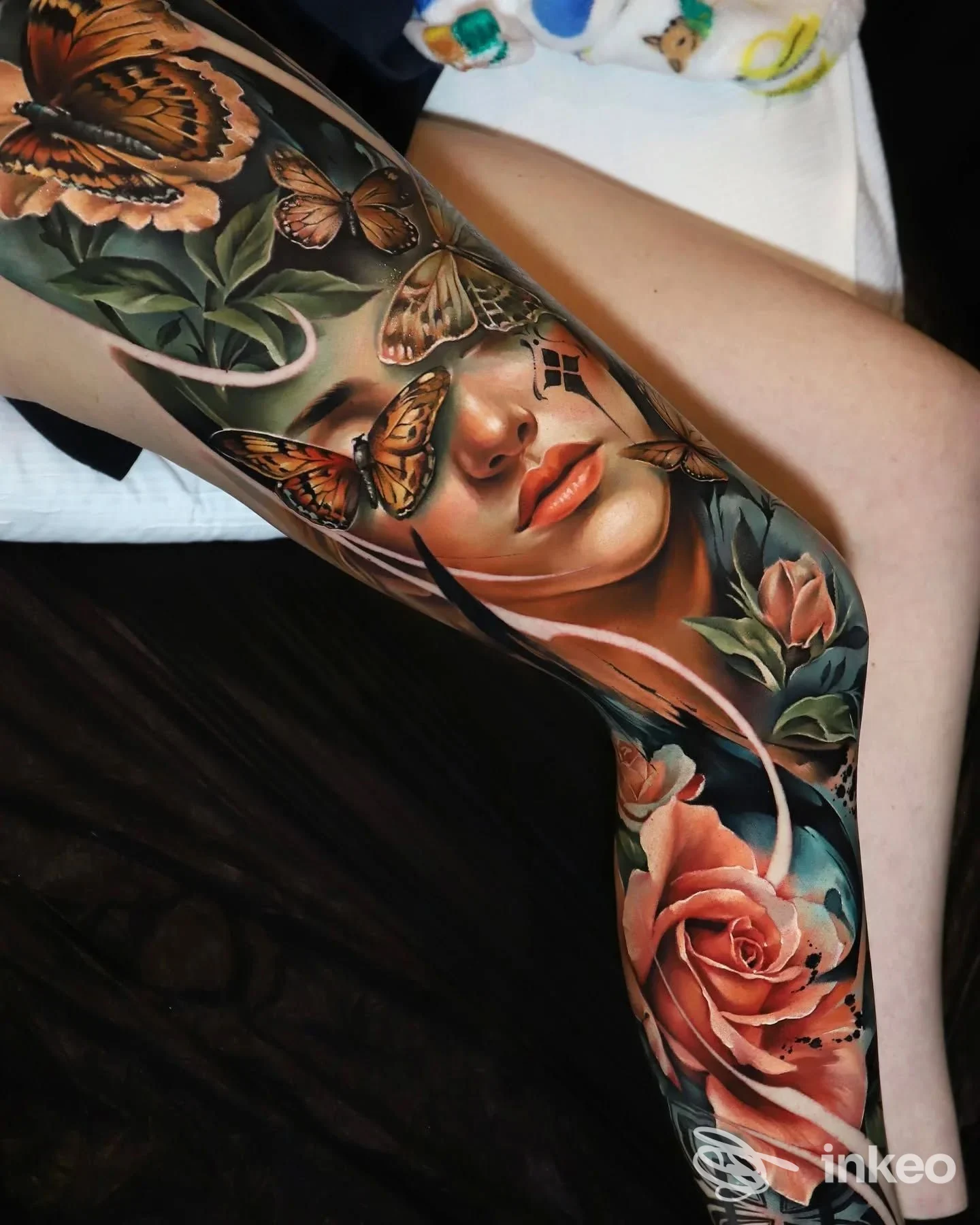 Tattoo realistico su pelle umana raffigurante una donna tra farfalle e rose, abbracciato dal braccio della modella; colori vividi e dettagli precisi, scatto singolo senza testo aggiunto.