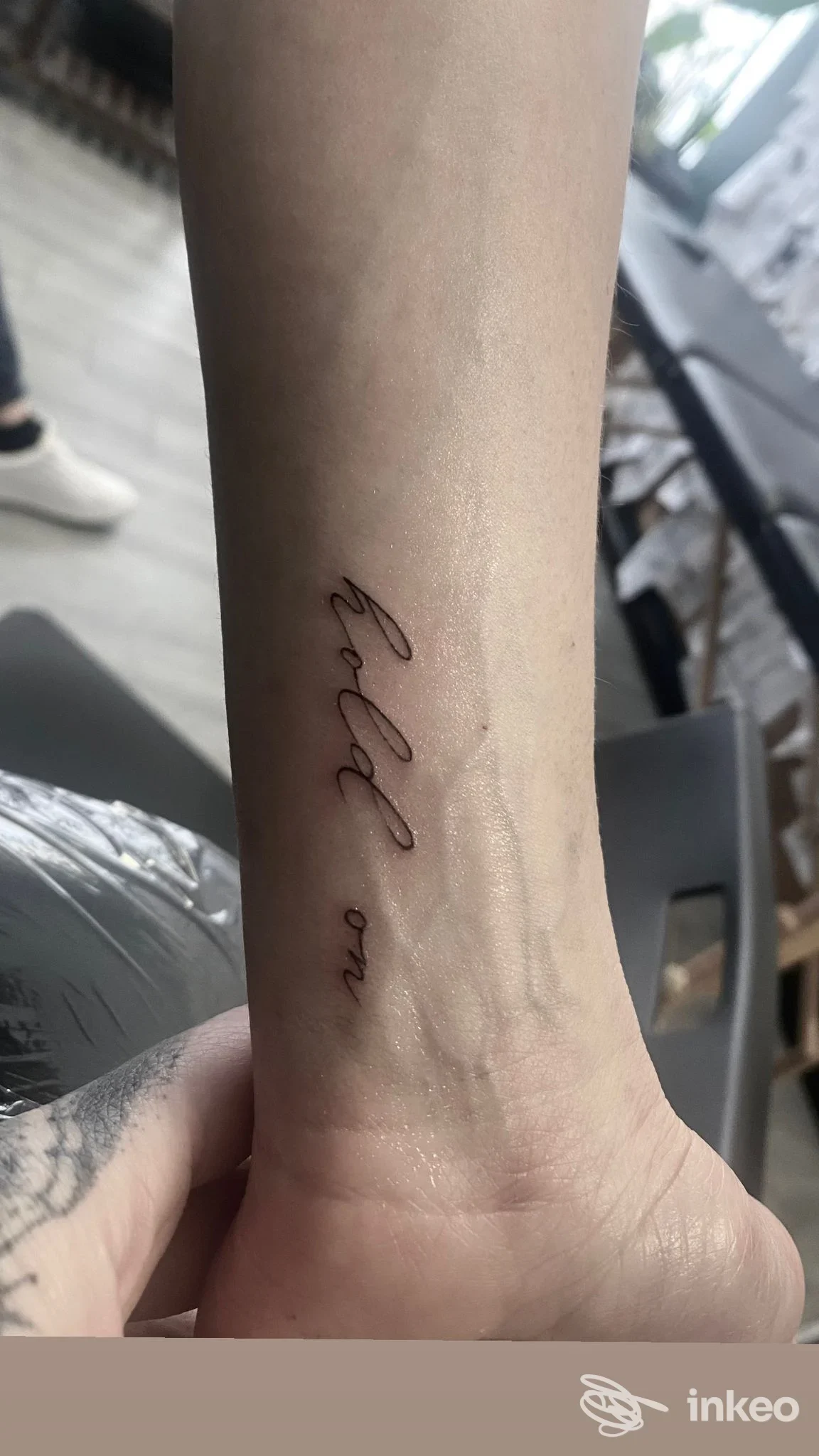 Tattoo script diagonale sul polso/avambraccio, inchiostro scuro su pelle, foto ravvicinata senza volto visibile.