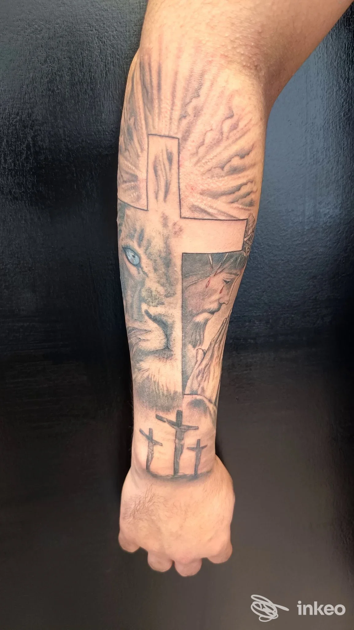Tattoo sull'avambraccio raffigurante una croce e motivi sfumati, in bianco e nero, senza volto visibile.