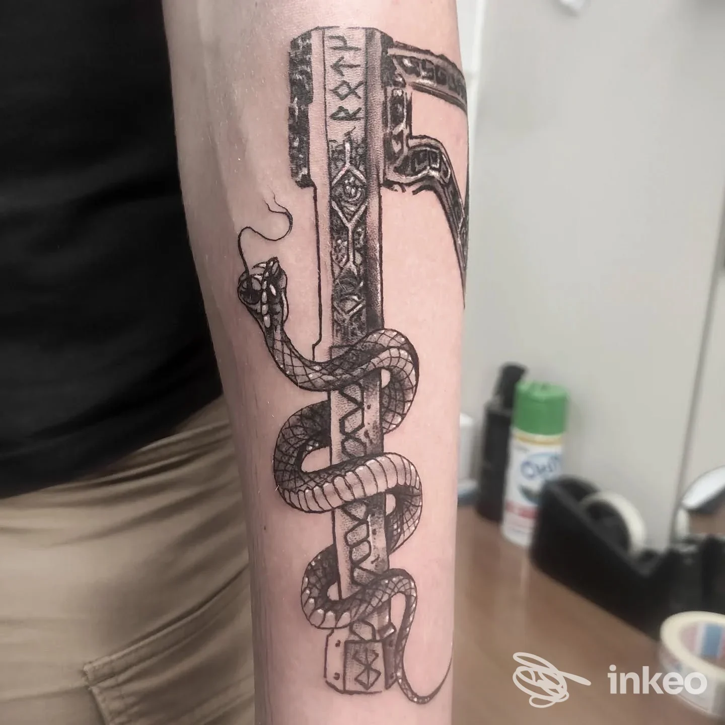 Tattoo su avambraccio raffigurante un serpente avvolgente intorno a una struttura verticale decorata, realizzato sulla pelle reale.